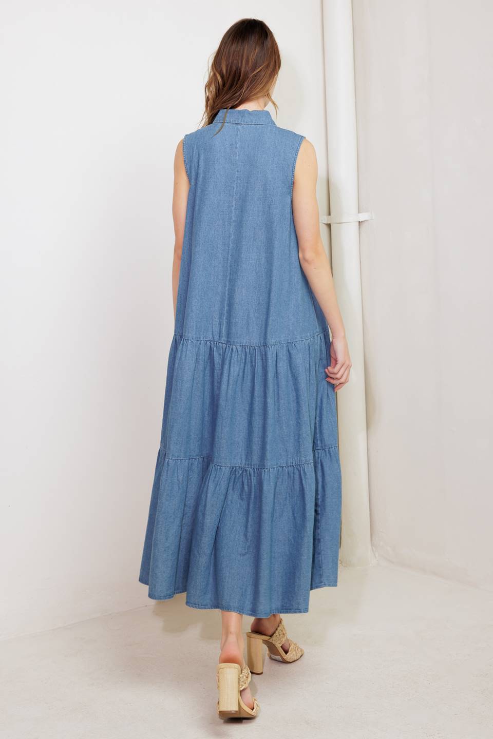 A washed denim midi dress featuring collar, snap button down, ruffled front, sleeveless, self sash tie and tiered skirt