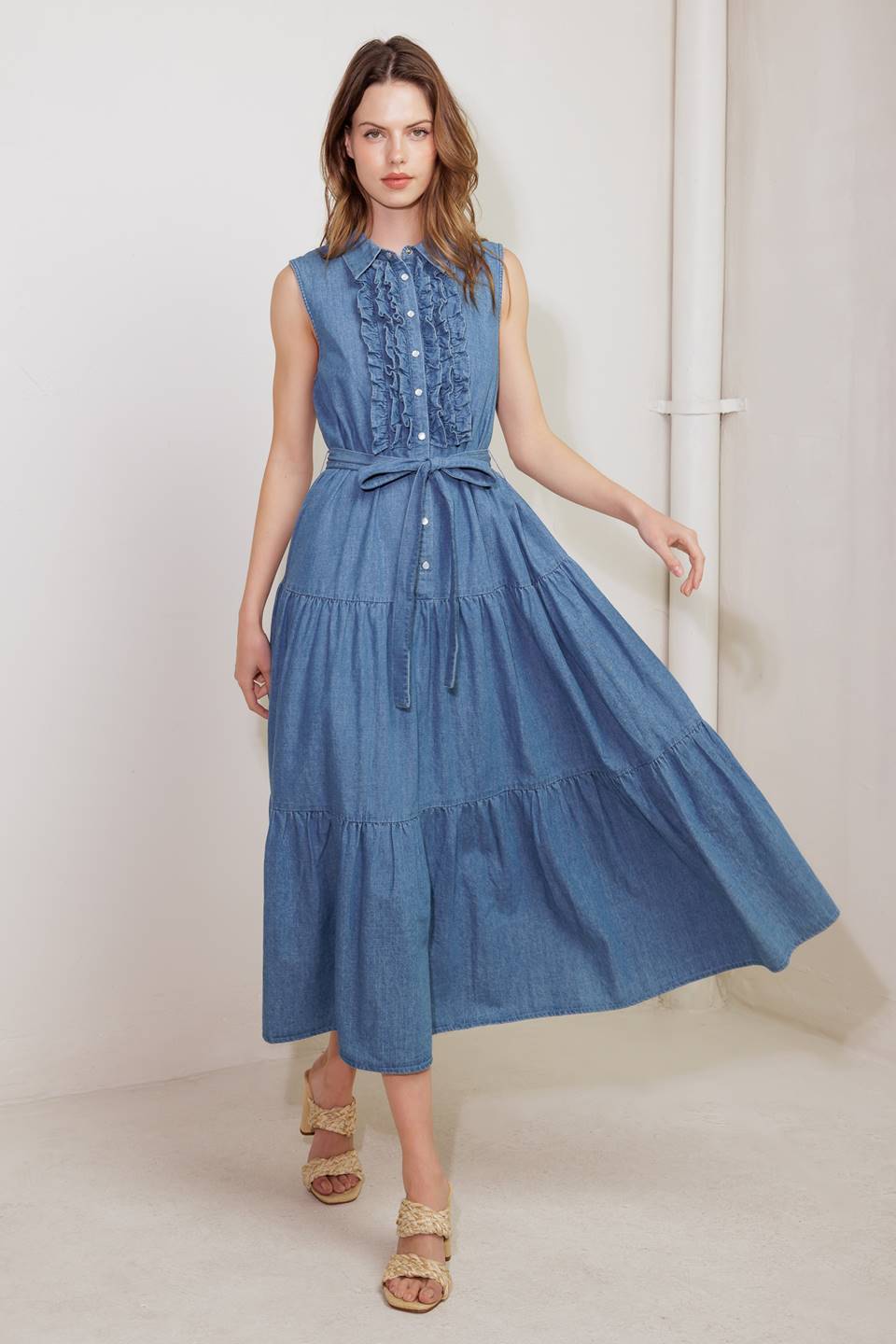 A washed denim midi dress featuring collar, snap button down, ruffled front, sleeveless, self sash tie and tiered skirt