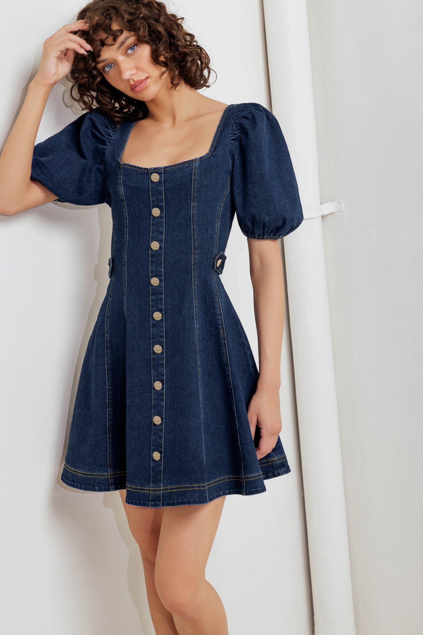 A washed denim mini dress featuring square neckline, short puff sleeve, button down detail, circle skirt and back zipper closure