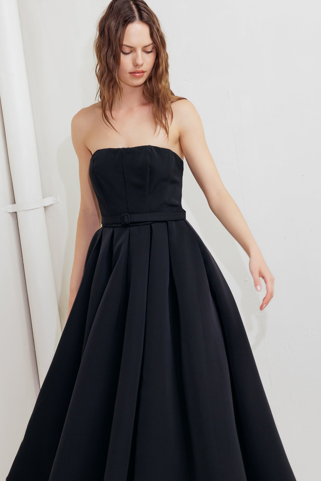 A solid woven midi dress featuring strapless straight neckline, self belt, full skirt and back zipper closure
