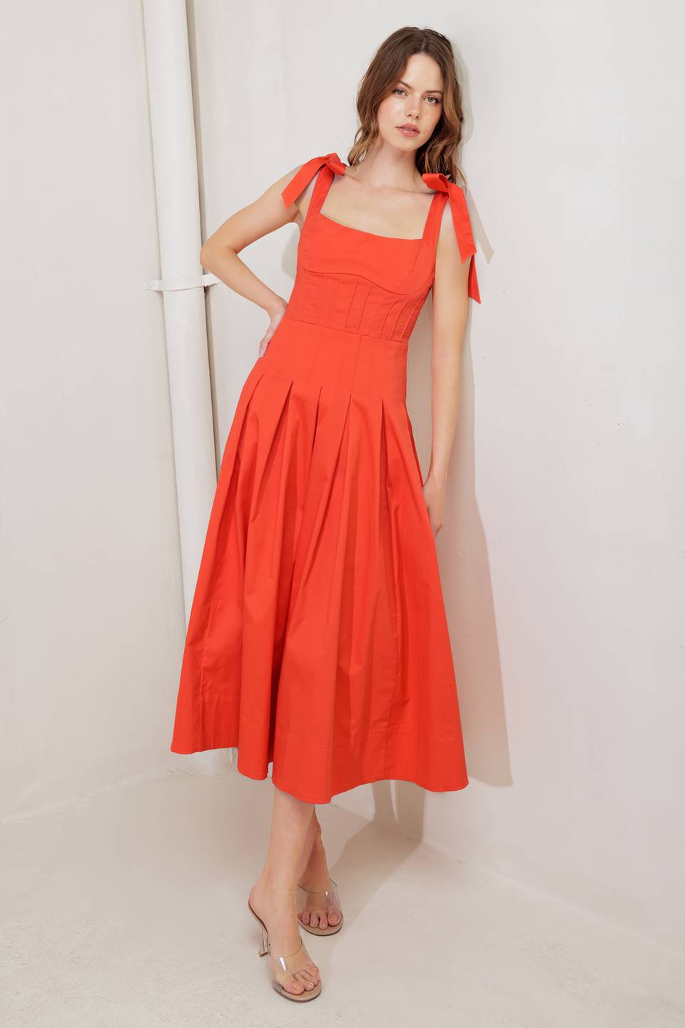 A solid red woven midi dress featuring straight neckline, shoulder ties, pintuck waist, inverted pleated skirt and bare back with straps and zipper closure