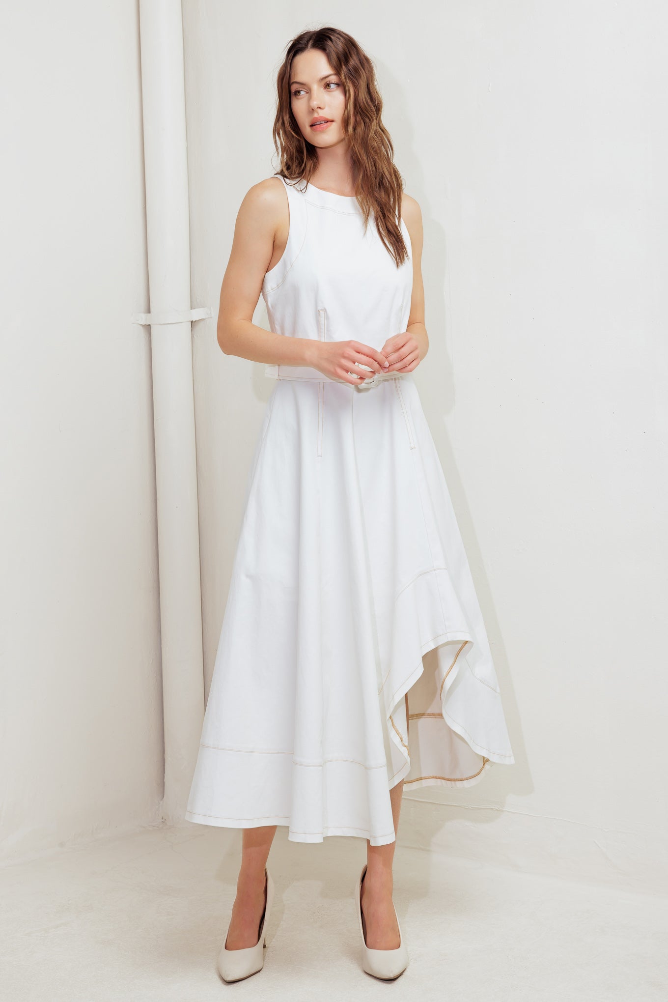A solid white woven midi dress featuring round neckline, sleeveless, self belt, circle skirt with side hi-lo and back zipper closure