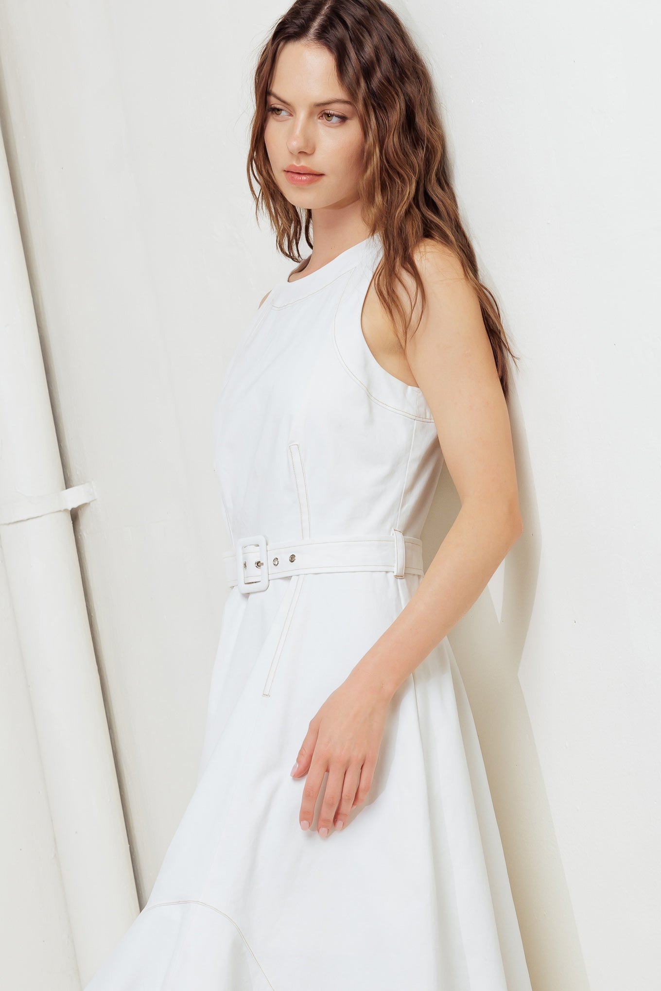 A solid white woven midi dress featuring round neckline, sleeveless, self belt, circle skirt with side hi-lo and back zipper closure