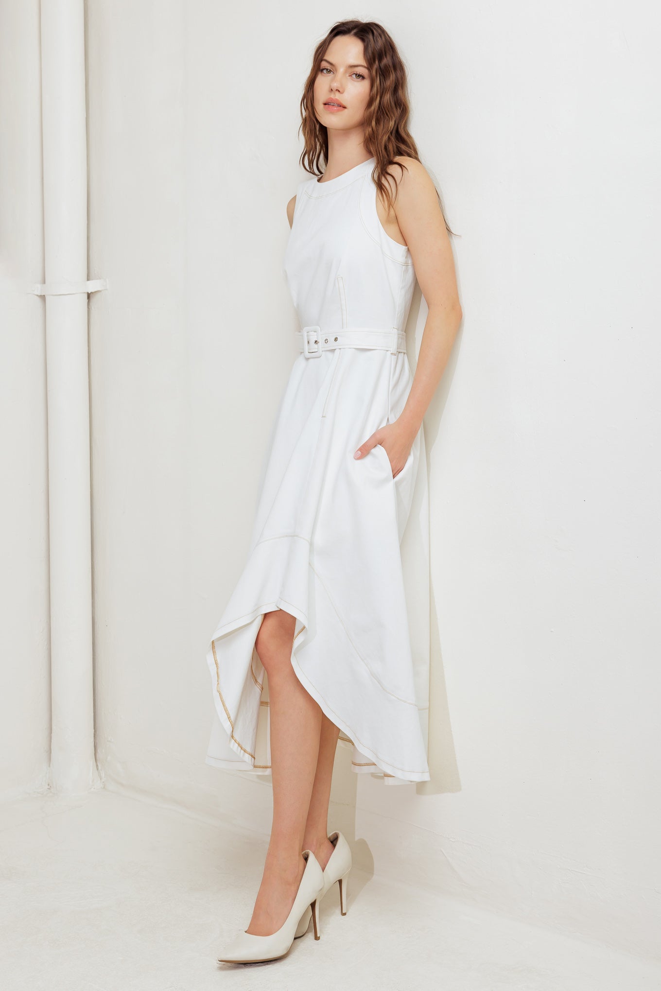 A solid white woven midi dress featuring round neckline, sleeveless, self belt, circle skirt with side hi-lo and back zipper closure
