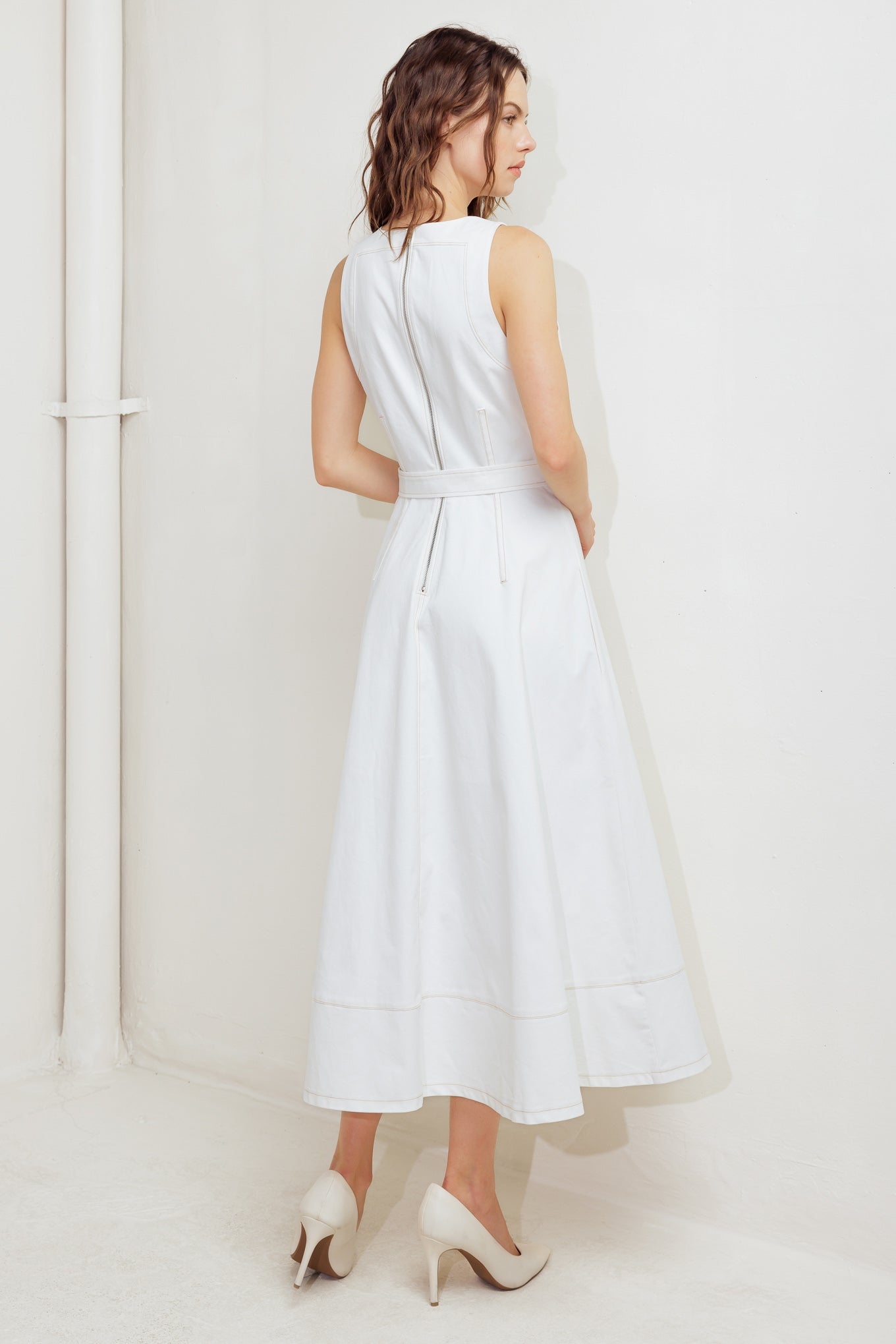 A solid white woven midi dress featuring round neckline, sleeveless, self belt, circle skirt with side hi-lo and back zipper closure