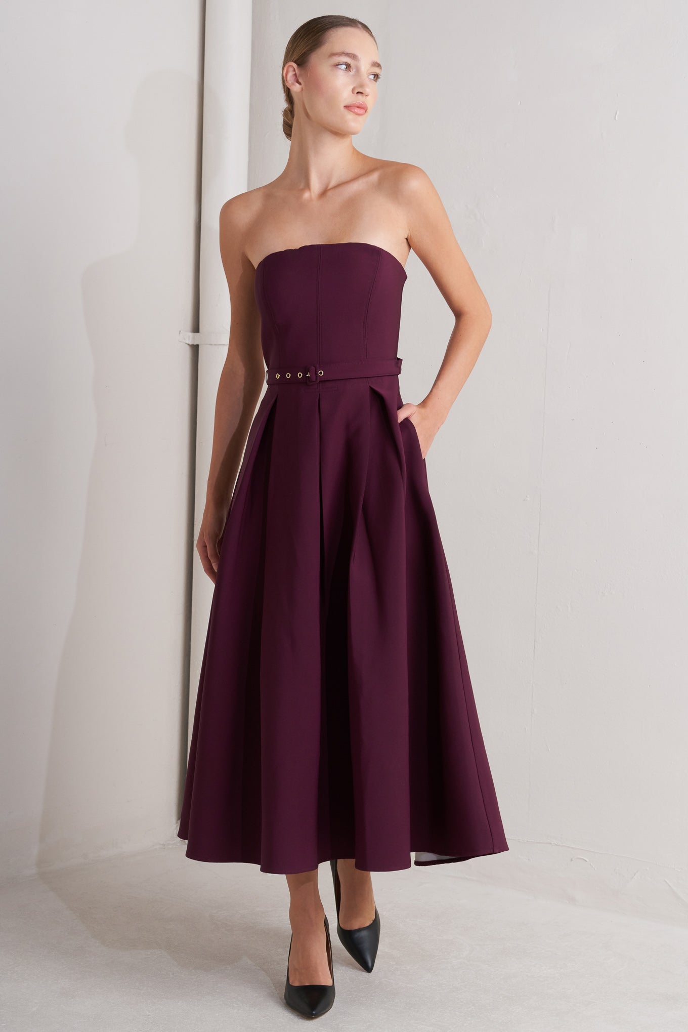 A solid woven mid dress featuring strapless, self belt, full skirt and back zipper closure