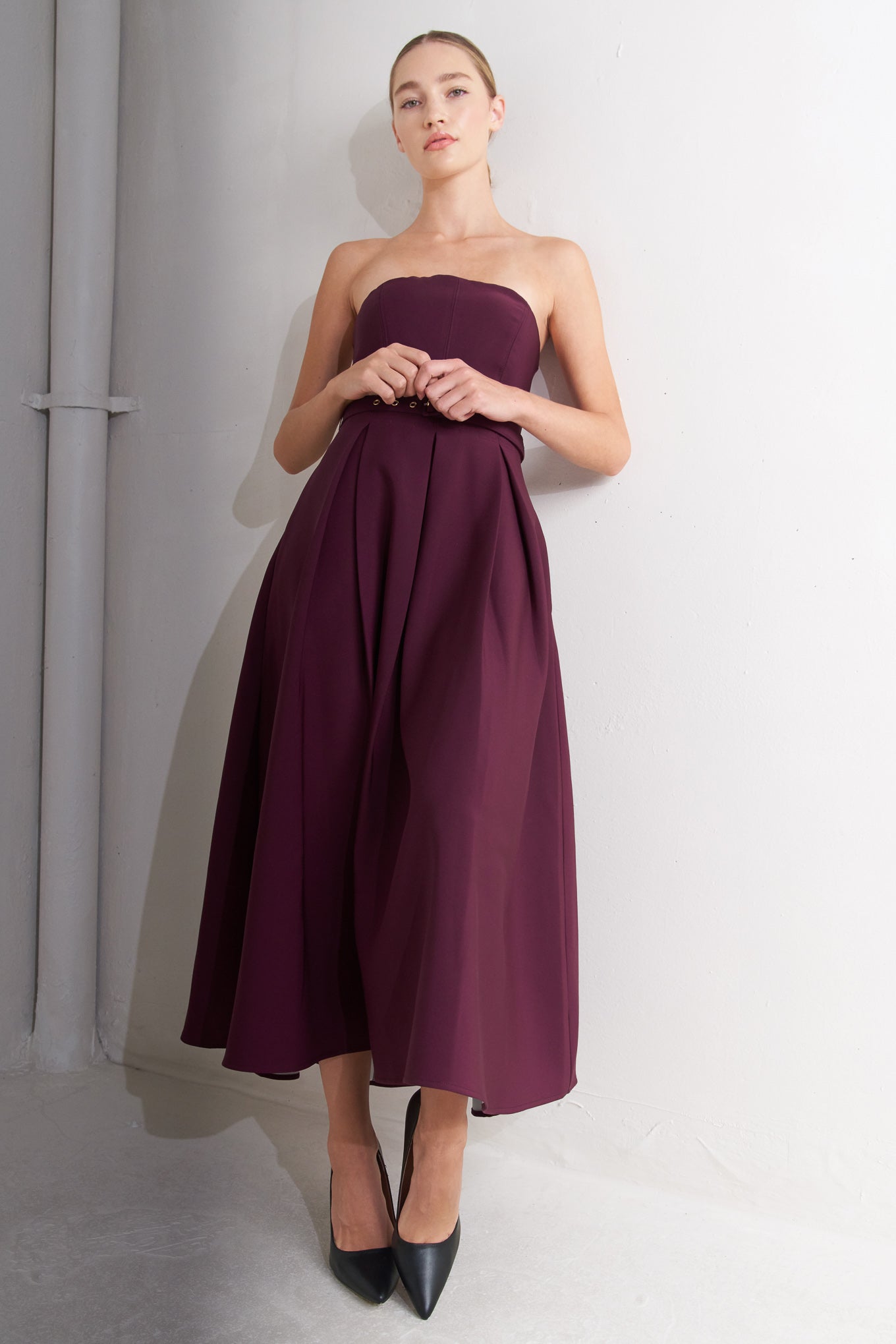 A solid woven mid dress featuring strapless, self belt, full skirt and back zipper closure