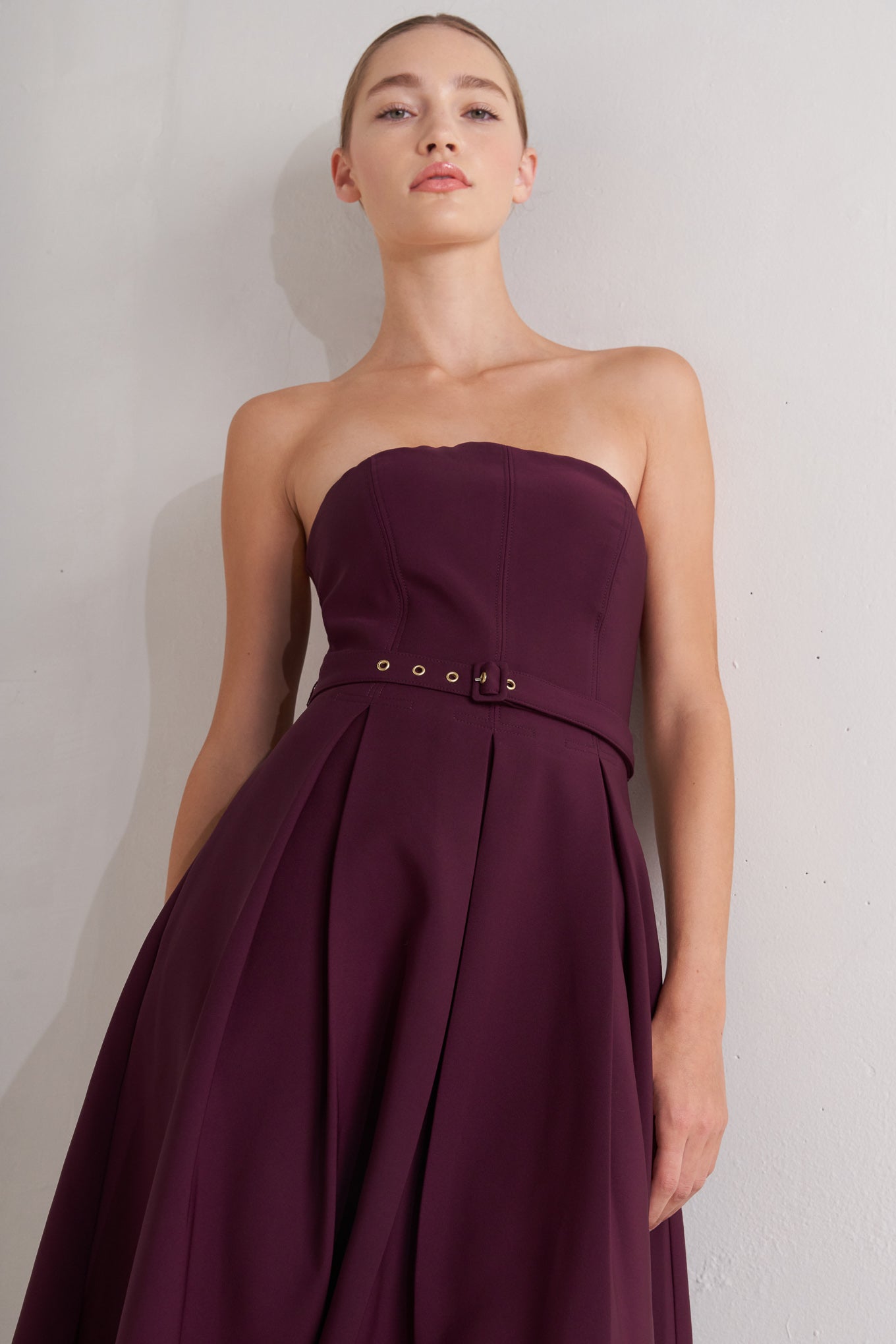 A solid woven mid dress featuring strapless, self belt, full skirt and back zipper closure