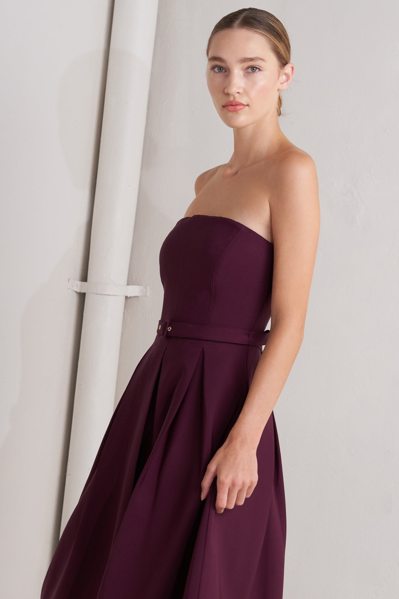 A solid woven mid dress featuring strapless, self belt, full skirt and back zipper closure