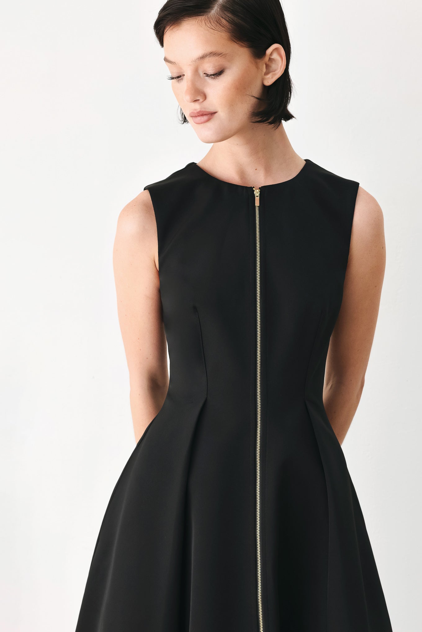 A woman modeling a sleeveless black midi dress with a prominent gold front zipper | FREEMARKET