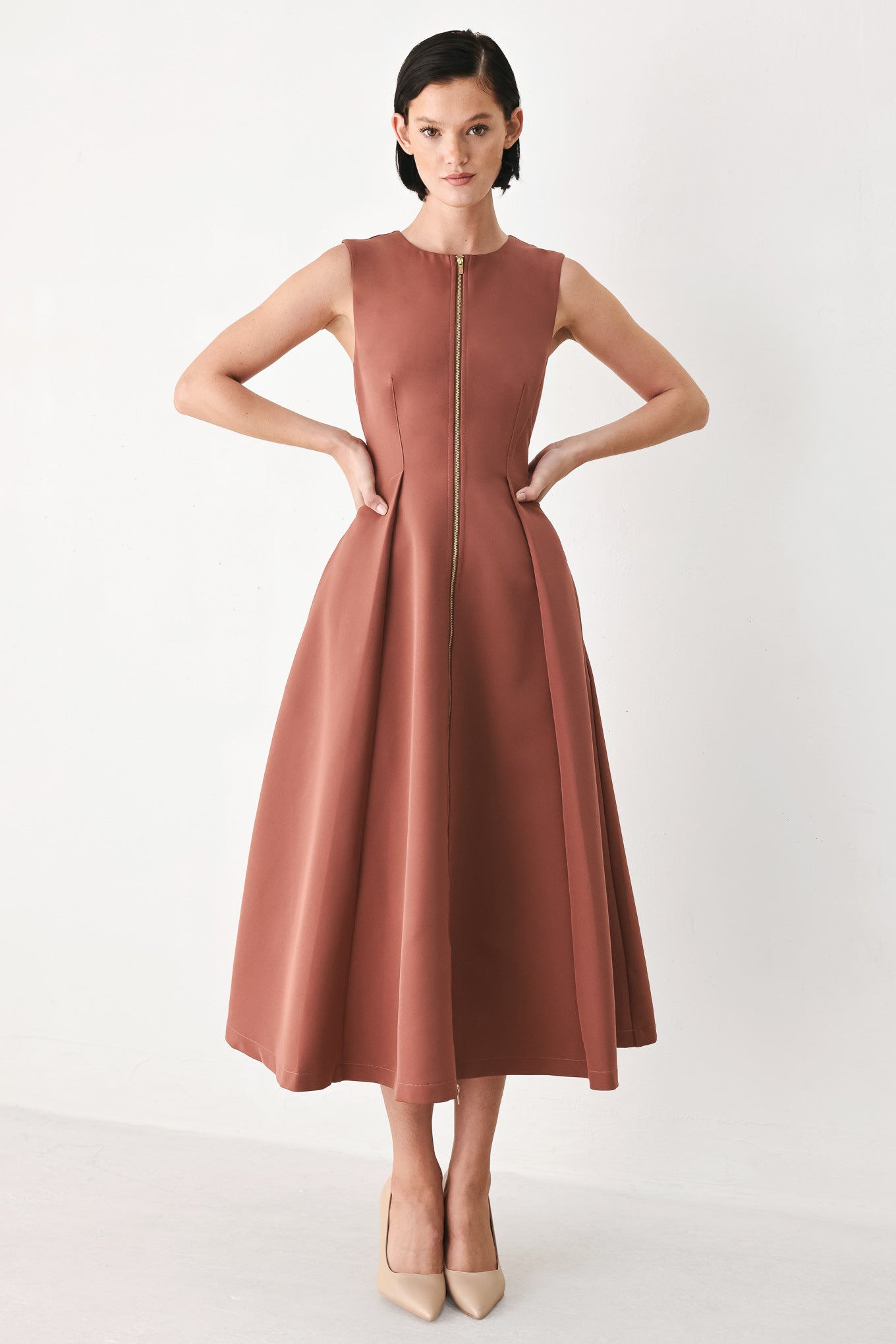 A woman modeling a sleeveless clay rose colored midi dress with a prominent gold front zipper | FREEMARKET