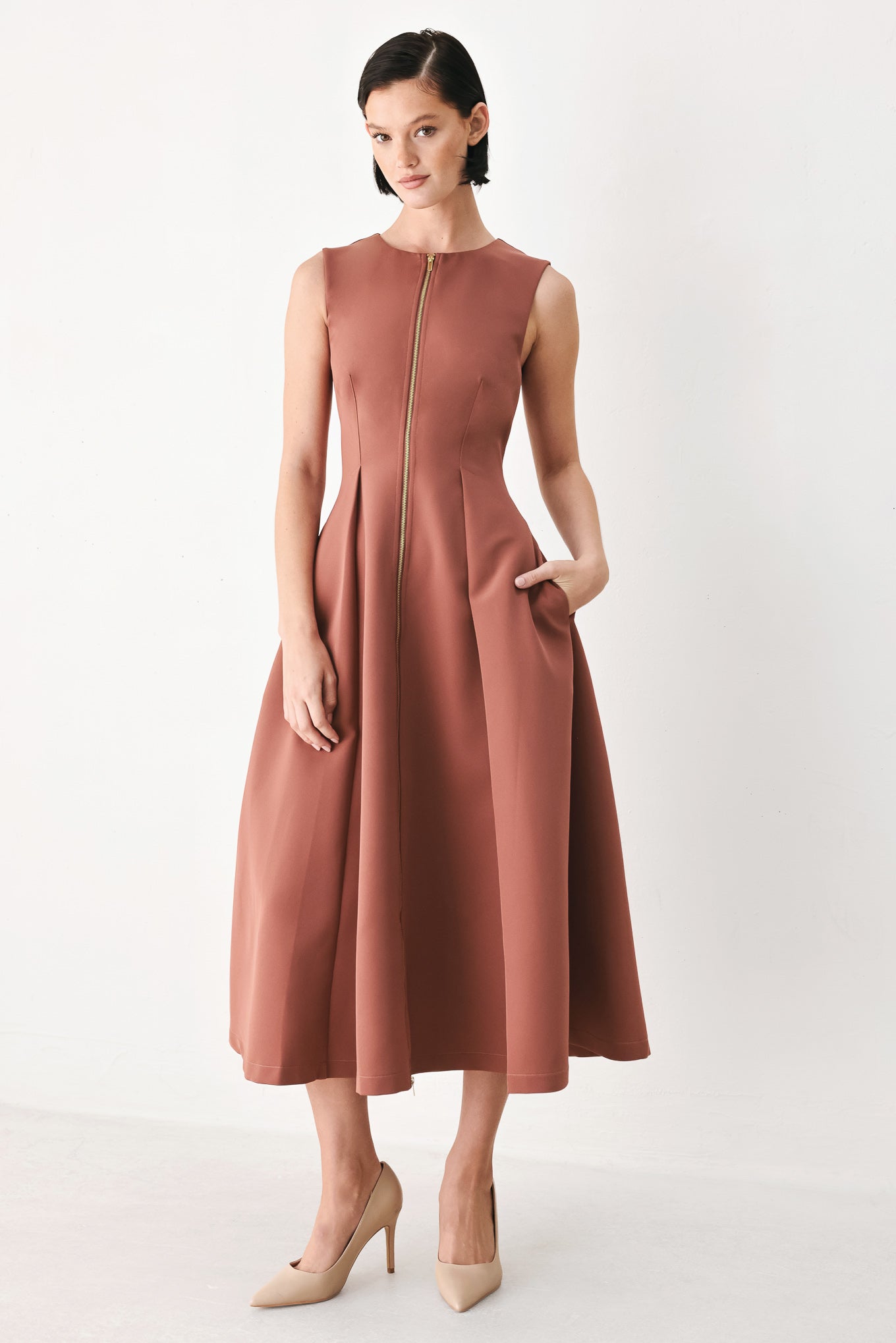 A woman modeling a sleeveless clay rose colored midi dress with a prominent gold front zipper | FREEMARKET