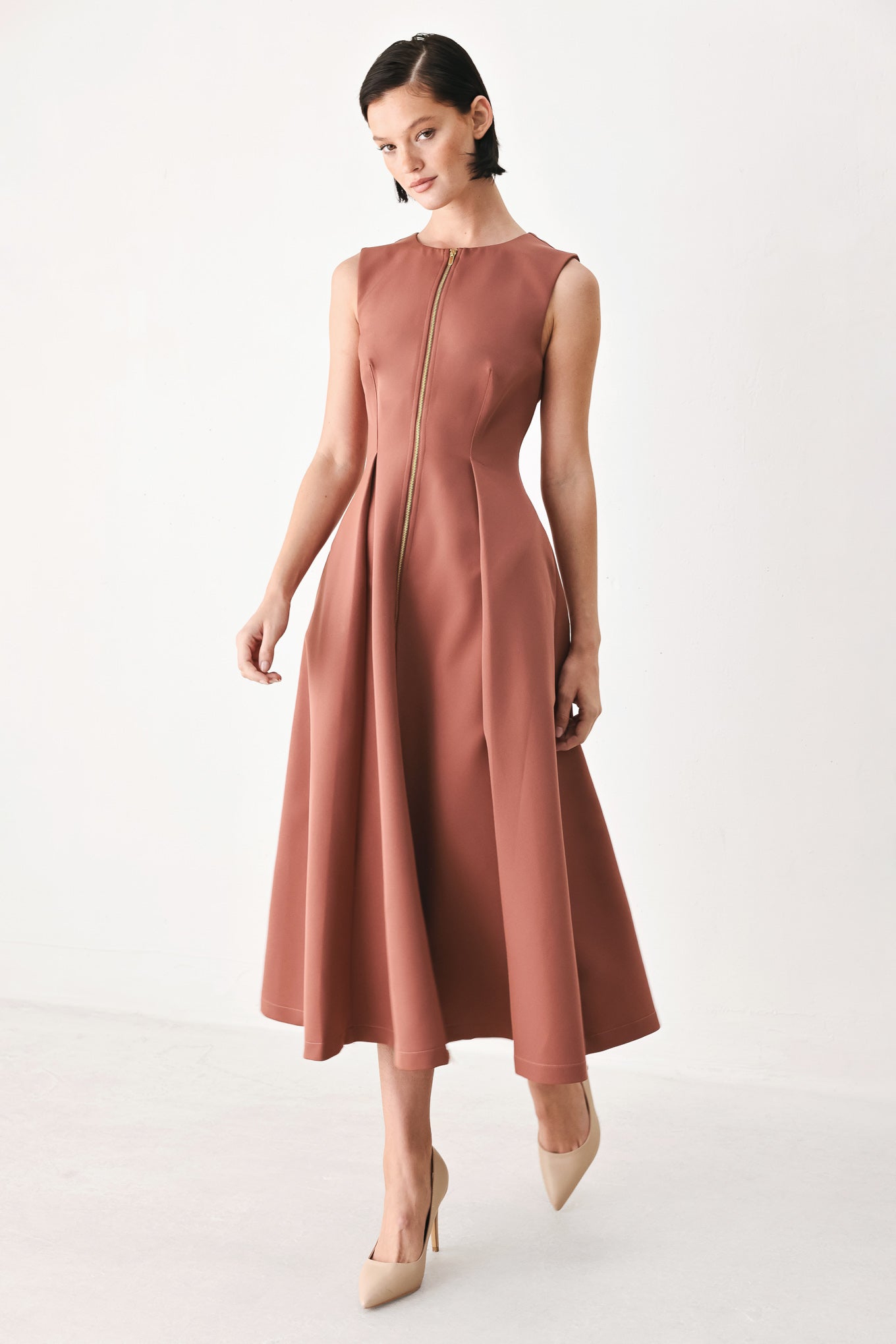 A woman modeling a sleeveless clay rose colored midi dress with a prominent gold front zipper | FREEMARKET