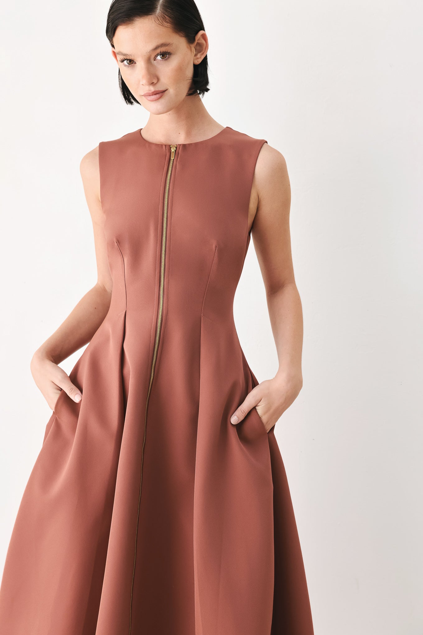 A woman modeling a sleeveless clay rose colored midi dress with a prominent gold front zipper | FREEMARKET