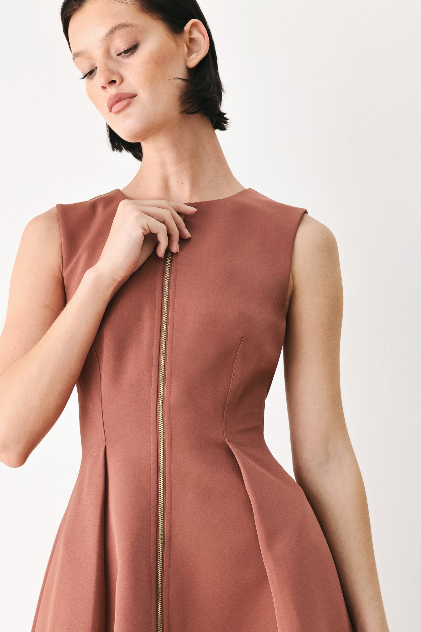 A woman modeling a sleeveless clay rose colored midi dress with a prominent gold front zipper | FREEMARKET