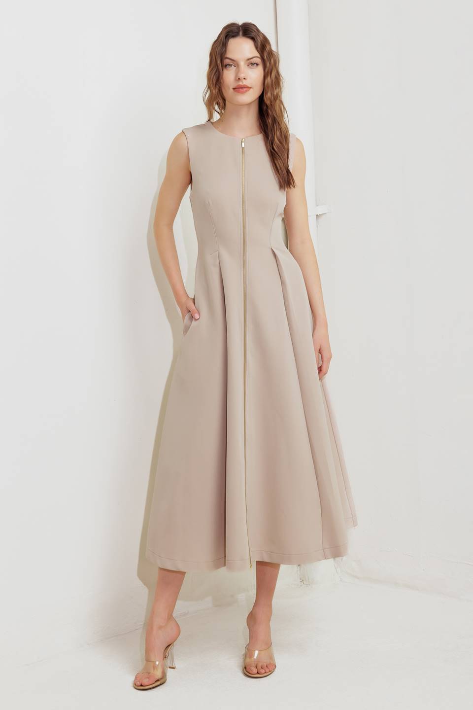 A woman modeling a sleeveless beige midi dress with a prominent gold front zipper | FREEMARKET
