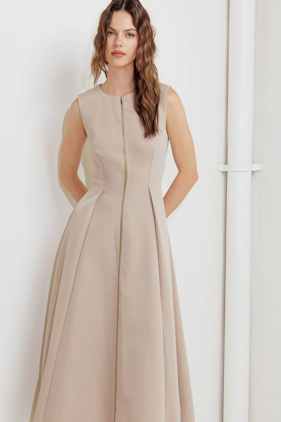 A woman modeling a sleeveless beige midi dress with a prominent gold front zipper | FREEMARKET