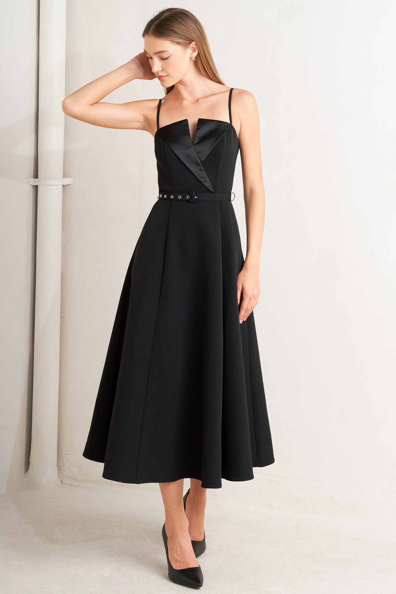 A solid woven midi dress featuring straight neckline with contrasting faux surplice lapel like detail, straps, self belt, circle skirt and back zipper closure