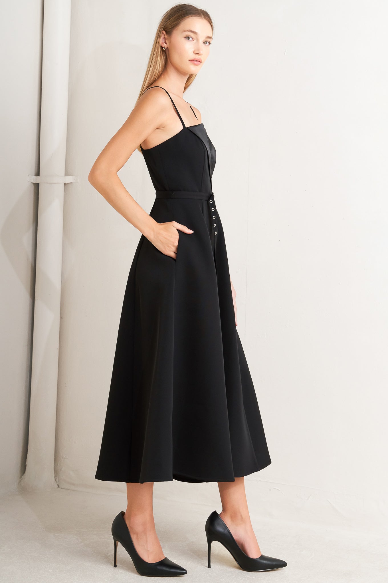 A solid woven midi dress featuring straight neckline with contrasting faux surplice lapel like detail, straps, self belt, circle skirt and back zipper closure