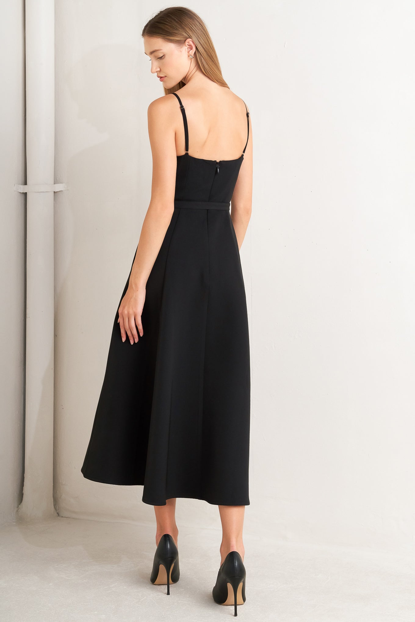 A solid woven midi dress featuring straight neckline with contrasting faux surplice lapel like detail, straps, self belt, circle skirt and back zipper closure