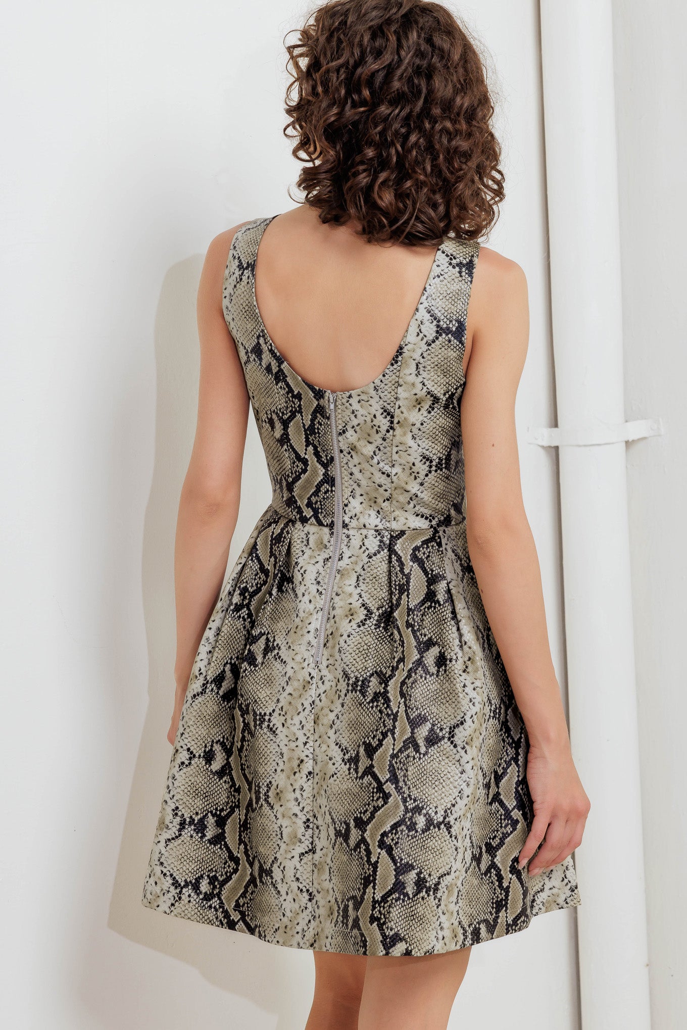 A printed faux leather mini dress featuring wide neckline, sleeveless, full skirt, U back and zipper closure