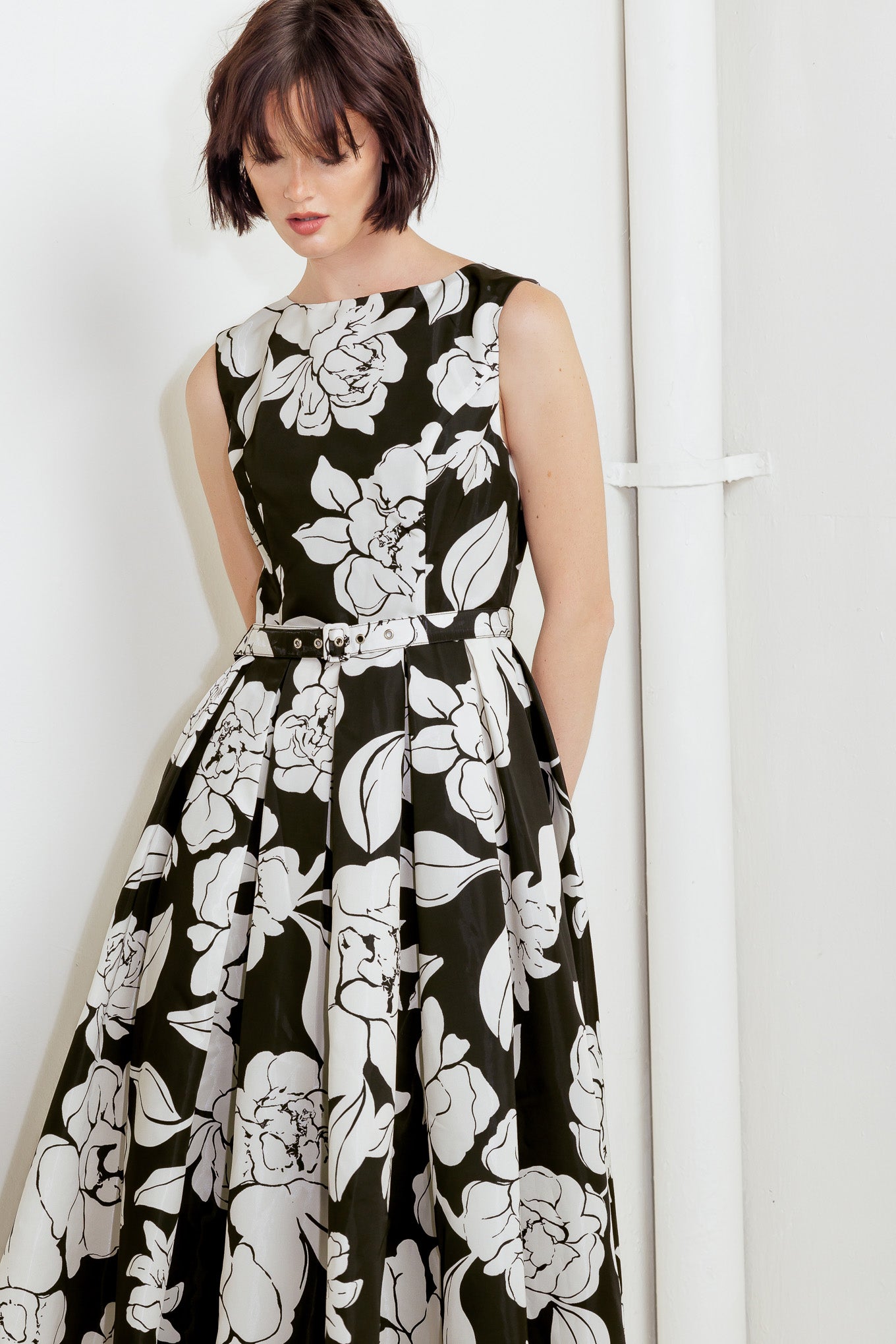 A printed woven midi dress featuring round neckline sleeveless, self belt, full skirt and back zipper closure
