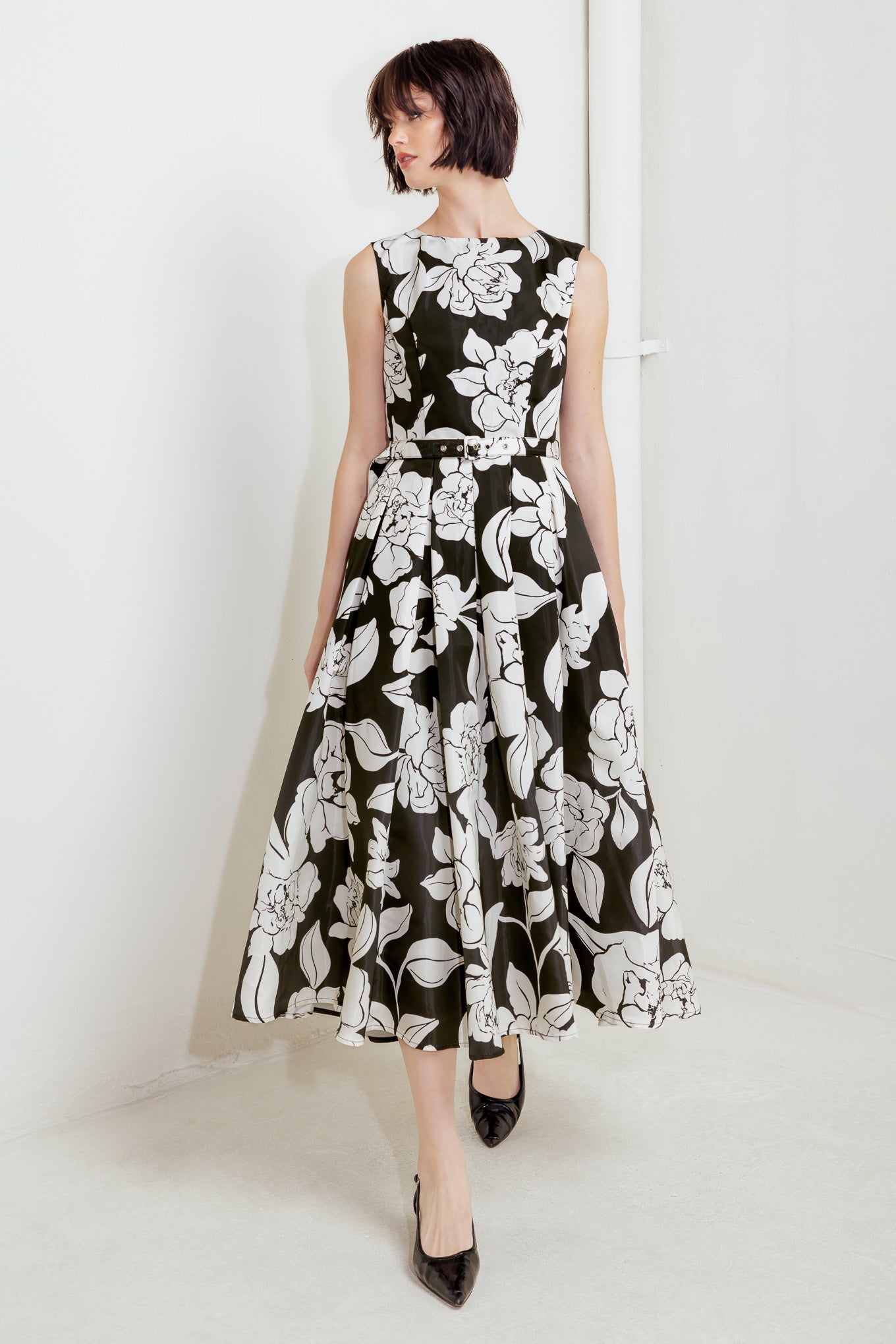 A printed woven midi dress featuring round neckline sleeveless, self belt, full skirt and back zipper closure