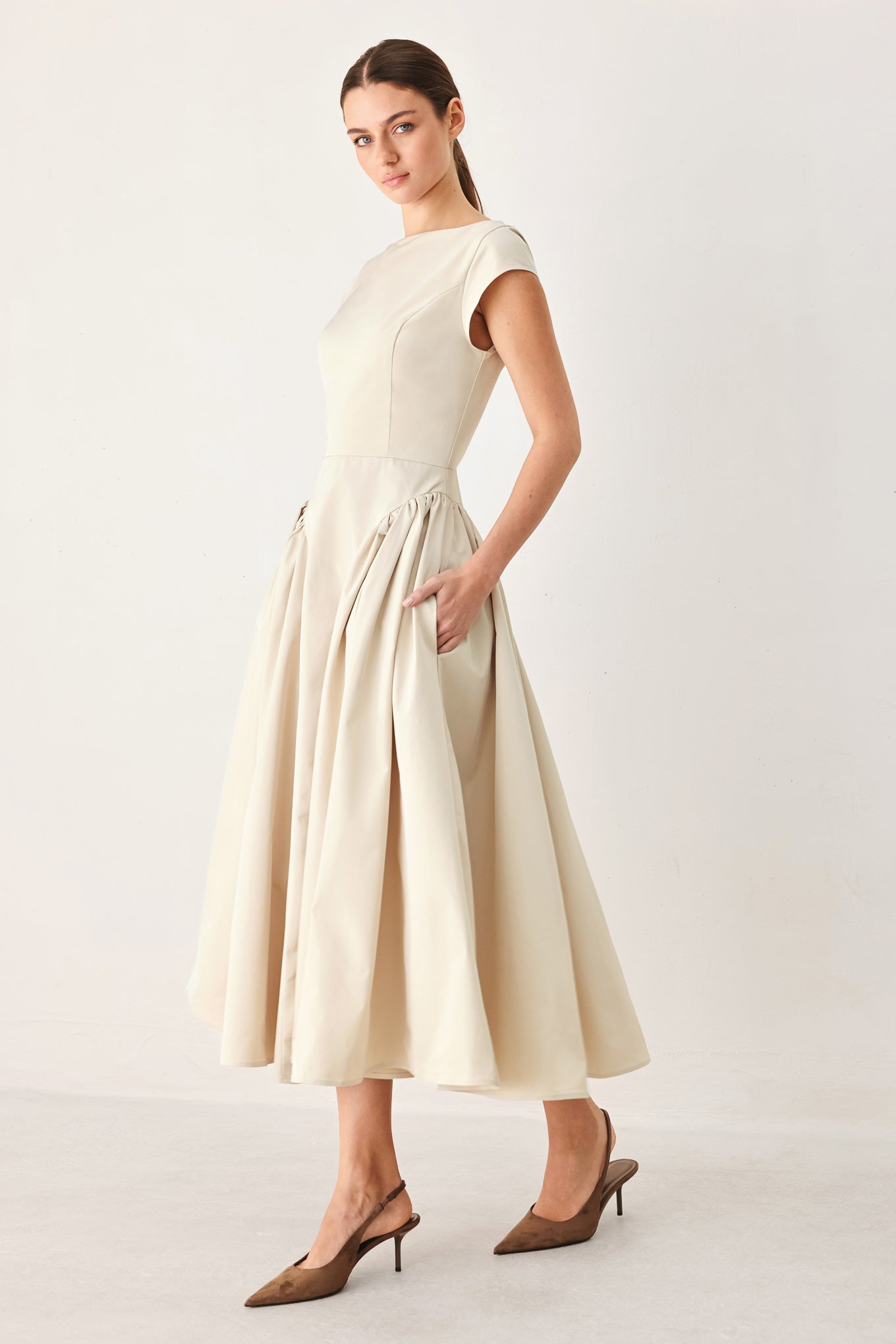 Woman wearing a solid light taupe woven midi dress featuring wide neckline, cap sleeve, side shirred full skirt, back cut out and button zipper closure | FREEMARKET