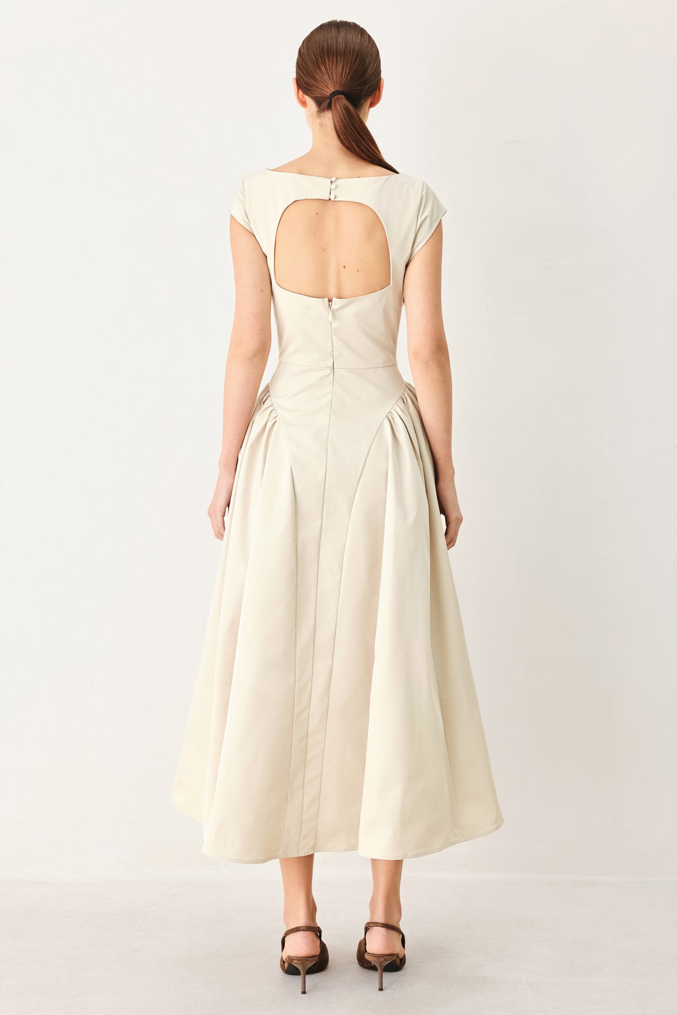 Woman wearing a solid light taupe woven midi dress featuring wide neckline, cap sleeve, side shirred full skirt, back cut out and button zipper closure | FREEMARKET