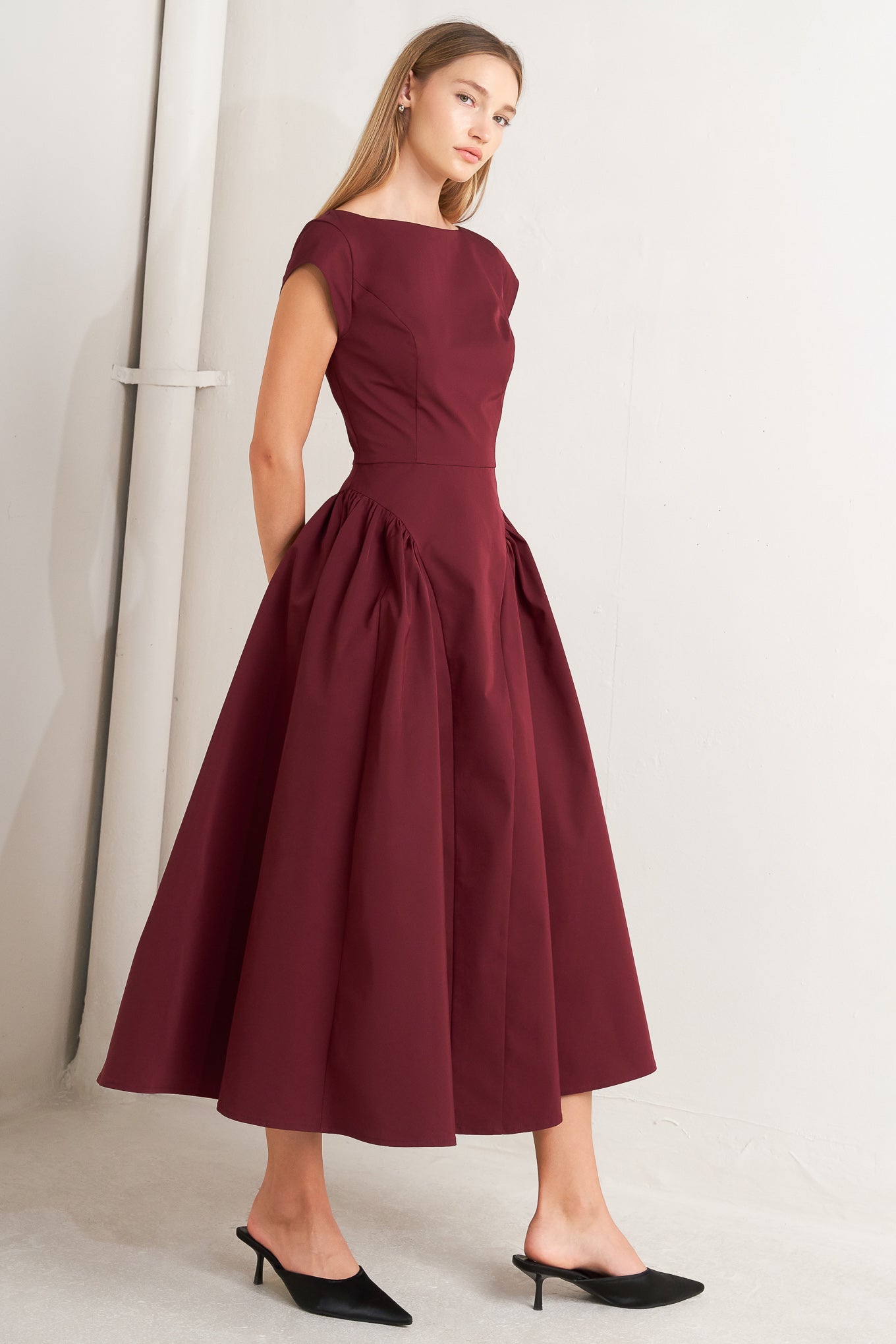 A solid woven midi dress featuring wide neckline, cap sleeve, side shirred full skirt, back cut out and button zipper closure