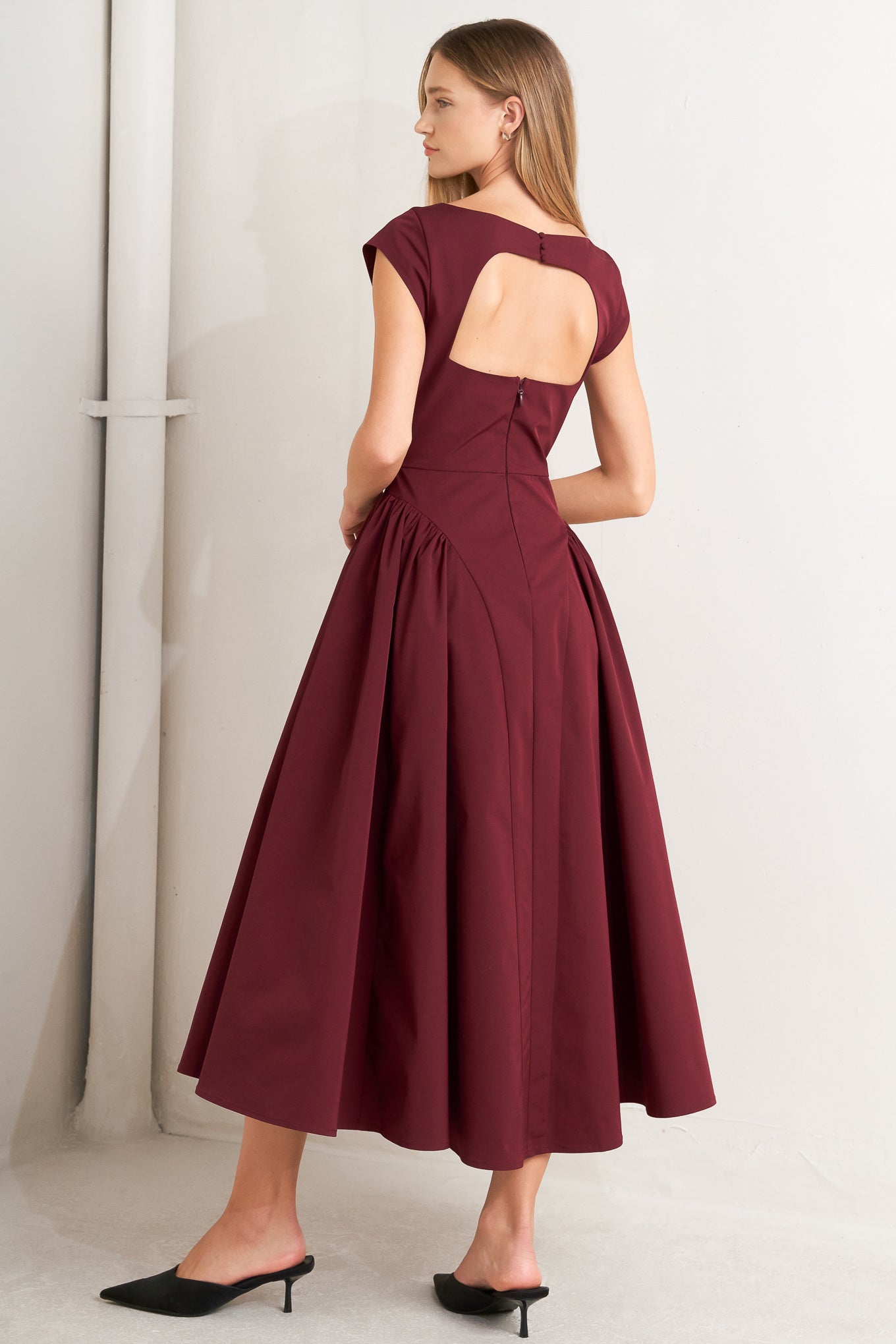 A solid woven midi dress featuring wide neckline, cap sleeve, side shirred full skirt, back cut out and button zipper closure