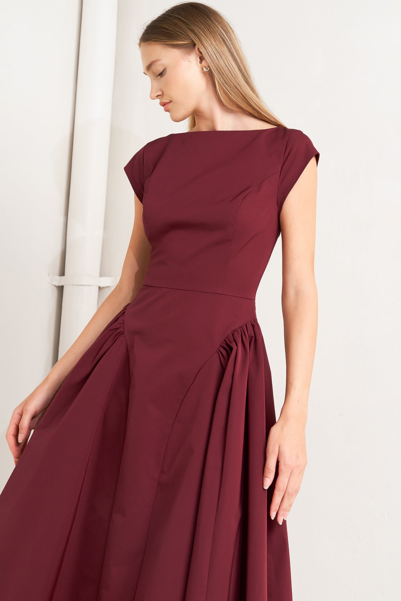 A solid woven midi dress featuring wide neckline, cap sleeve, side shirred full skirt, back cut out and button zipper closure
