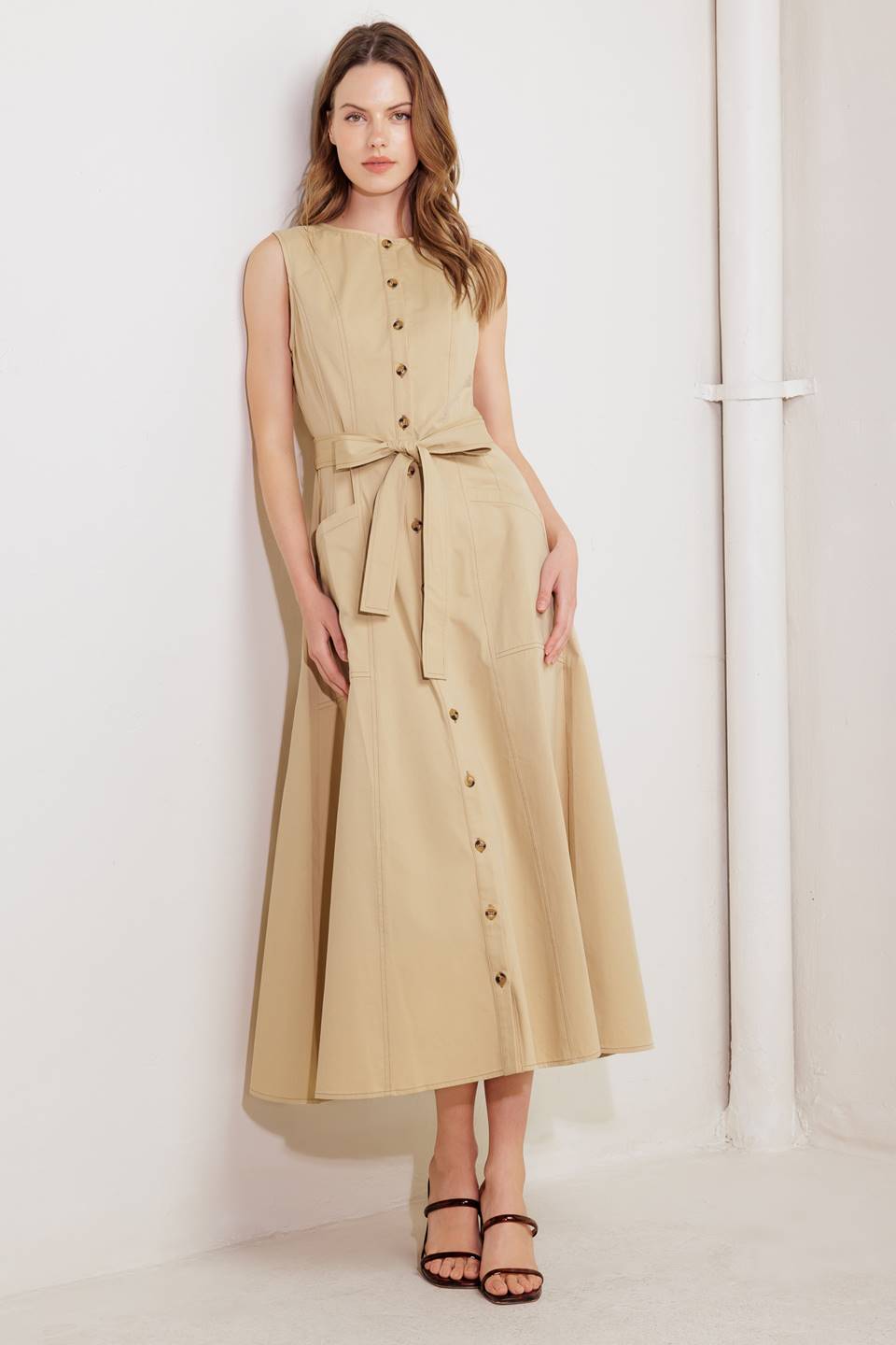 A solid woven midi dress featuring round neckline, sleeveless, button down, self sash tie, side pocket and circle skirt