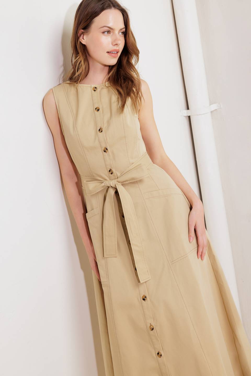 A solid woven midi dress featuring round neckline, sleeveless, button down, self sash tie, side pocket and circle skirt