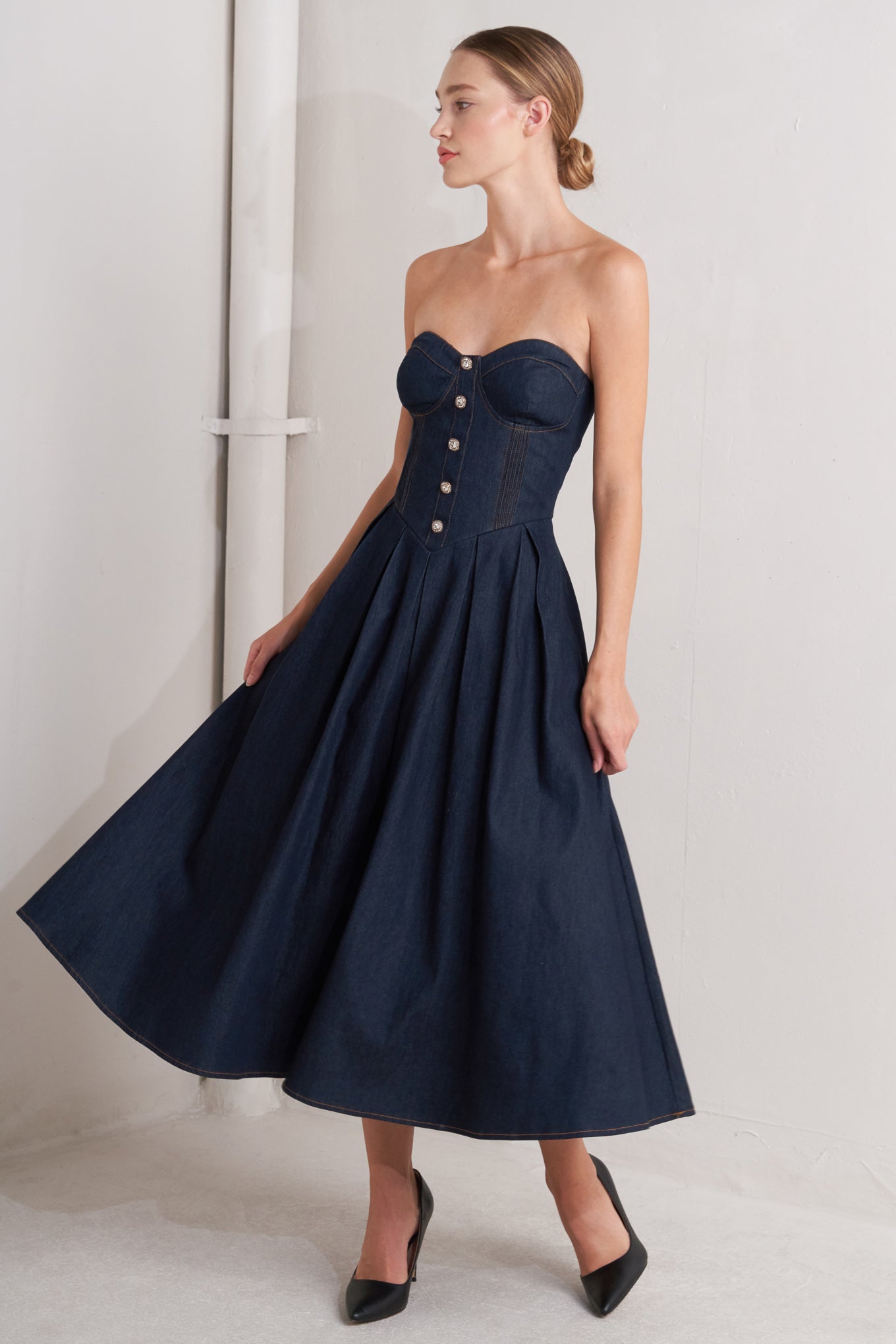 A denim midi dress featuring strapless sweetheart neckline, bustier bodice with button detail, basque waist, full skirt and back zipper closure