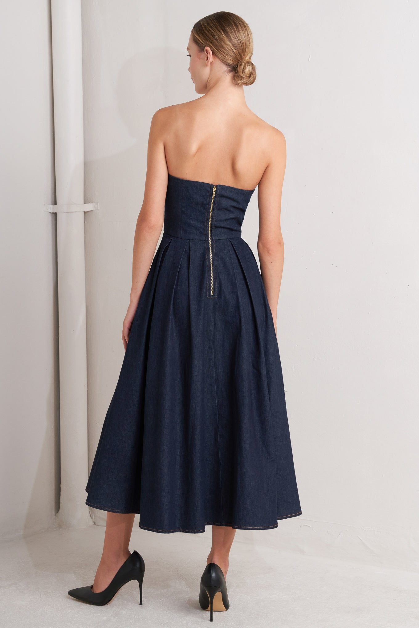 A denim midi dress featuring strapless sweetheart neckline, bustier bodice with button detail, basque waist, full skirt and back zipper closure