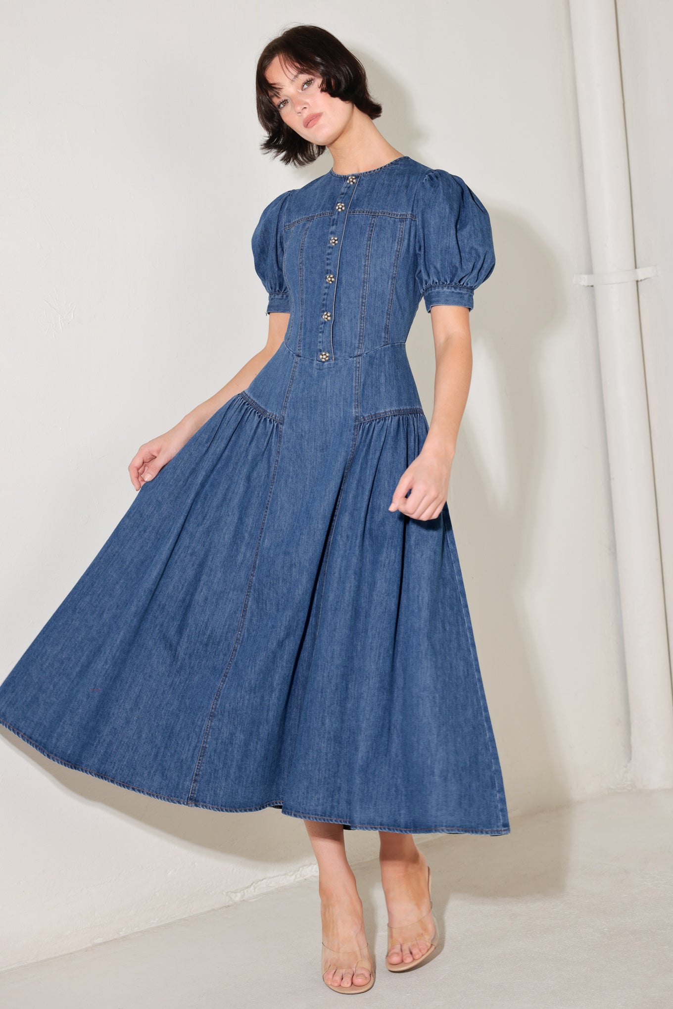 
A washed denim midi dress featuring round neckline, short puff sleeve, jewel button down, side shirring detail. full skirt and back zipper closure

Details:

Self : 85% Cotton 15% Polyester

Size &amp; Fit

- Model is 5`8" And Wearing Size Small
- Measurements Taken From Size Small
- Approx. Length: 50"