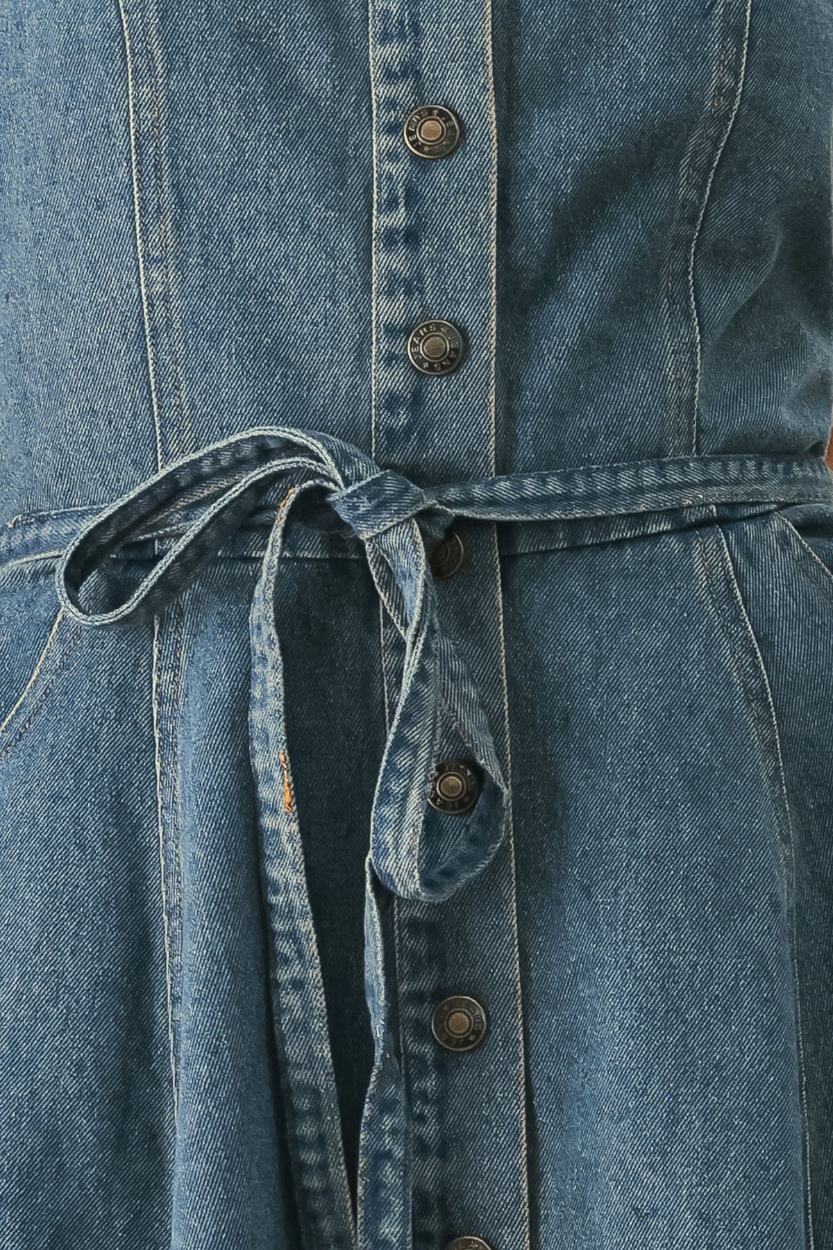 A woman modeling a strapless high-low denim dress in a dusty blue wash. The dress features a buttoned bodice, a matching fabric tie belt at the waist, and a flared skirt with an asymmetrical high-low hem. | FREEMARKET