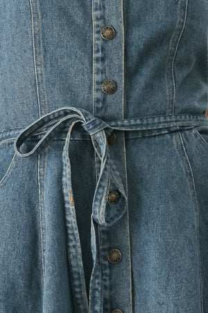 A woman modeling a strapless high-low denim dress in a dusty blue wash. The dress features a buttoned bodice, a matching fabric tie belt at the waist, and a flared skirt with an asymmetrical high-low hem. | FREEMARKET