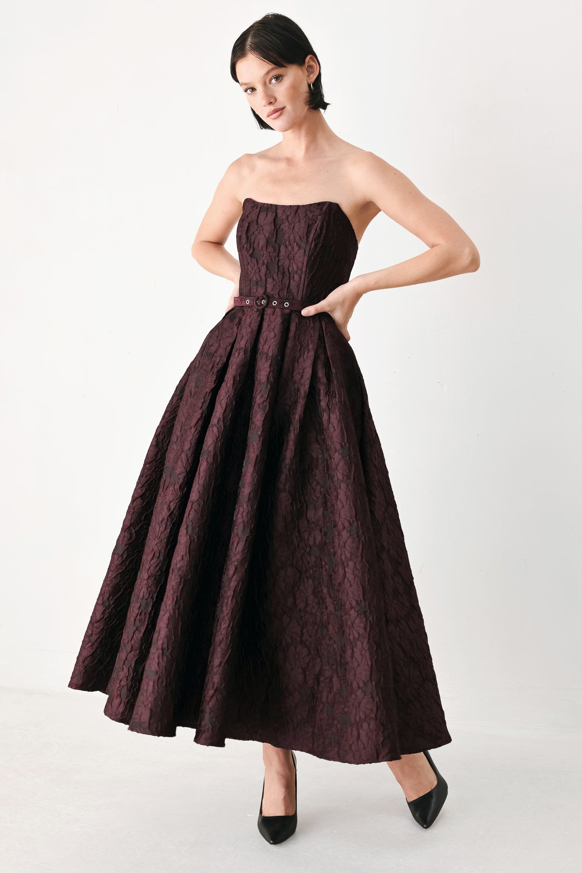A woman models a strapless burgundy A-line gown with a textured jacquard bodice and a matching beaded waistband | FREEMARKET