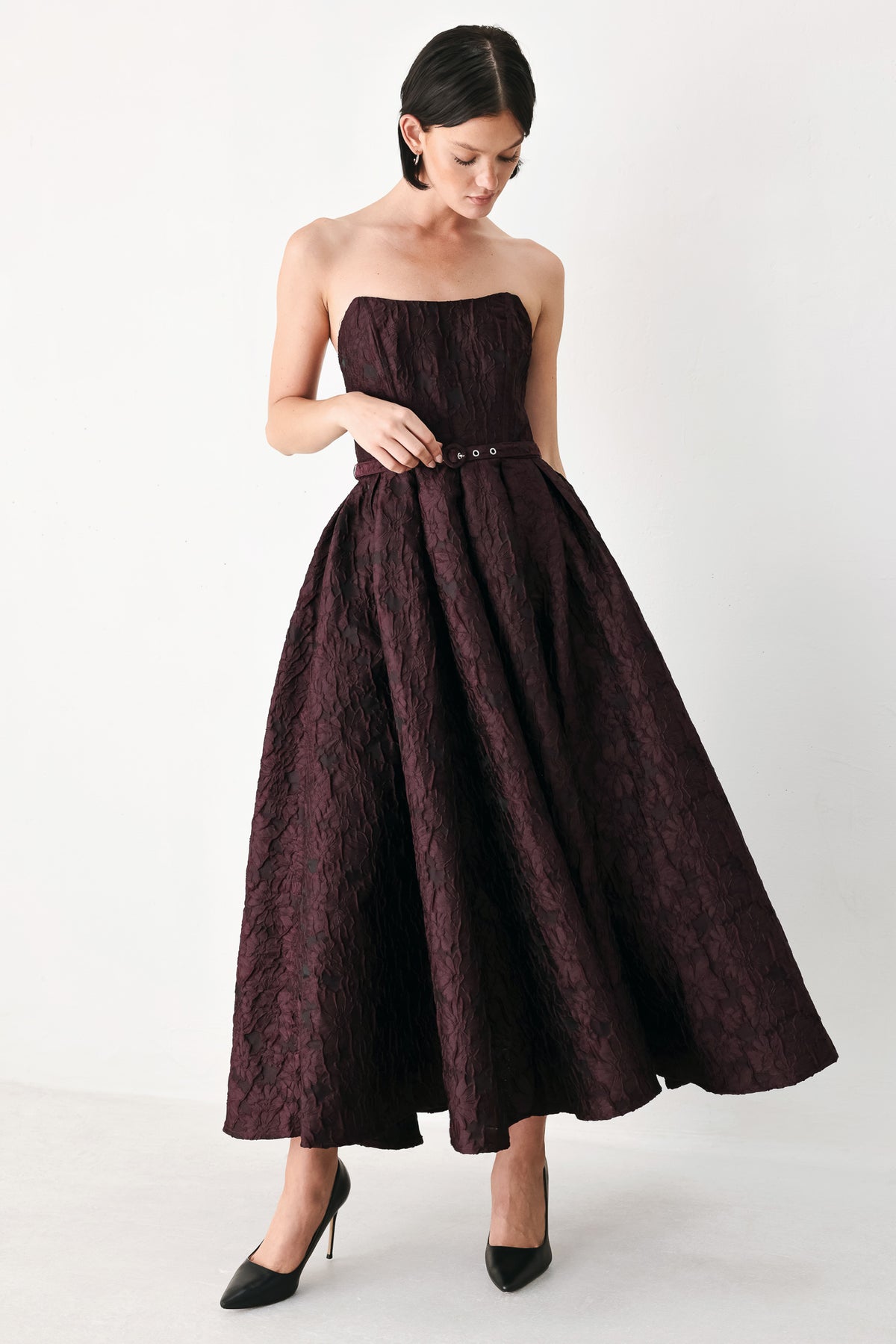A woman models a strapless burgundy A-line gown with a textured jacquard bodice and a matching beaded waistband | FREEMARKET