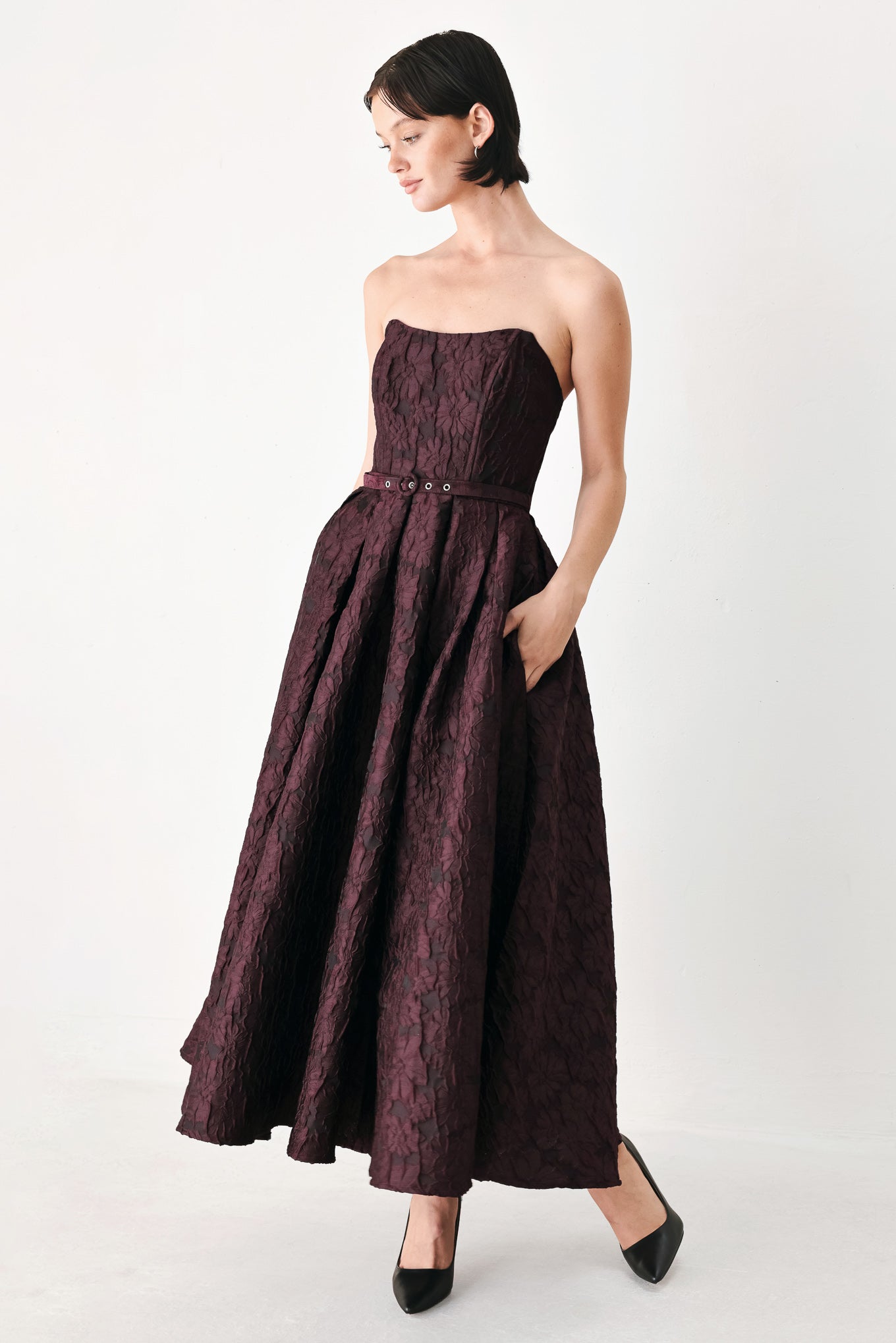 A woman models a strapless burgundy A-line gown with a textured jacquard bodice and a matching beaded waistband | FREEMARKET