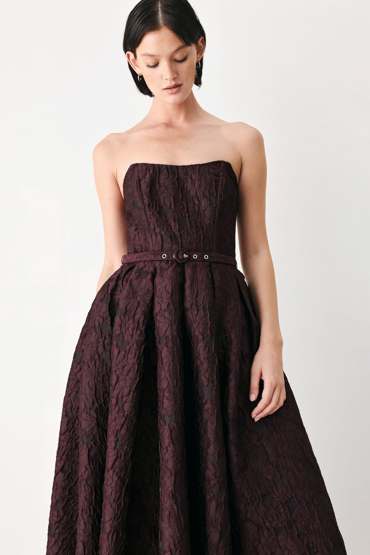 A woman models a strapless burgundy A-line gown with a textured jacquard bodice and a matching beaded waistband | FREEMARKET