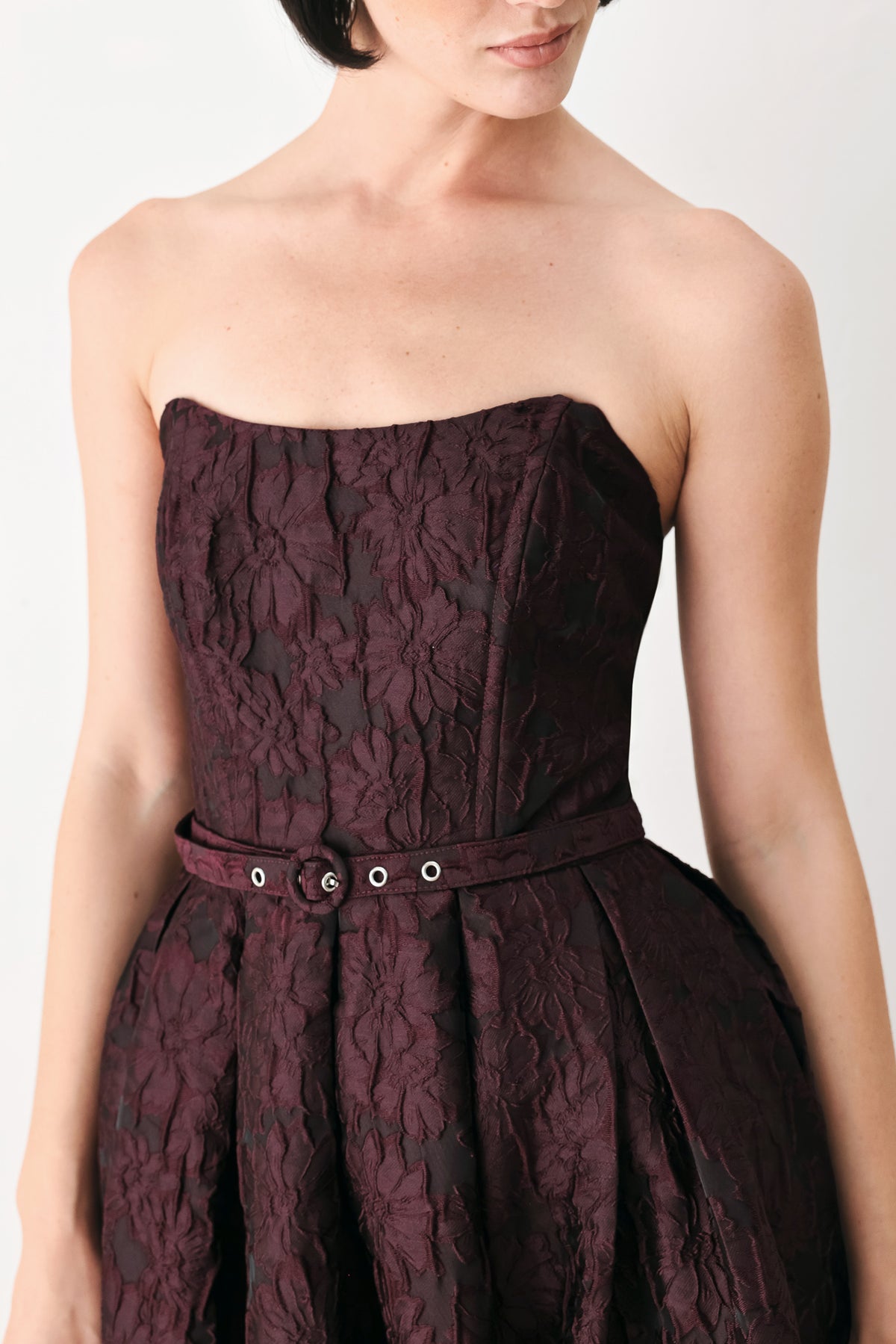 A woman models a strapless burgundy A-line gown with a textured jacquard bodice and a matching beaded waistband | FREEMARKET
