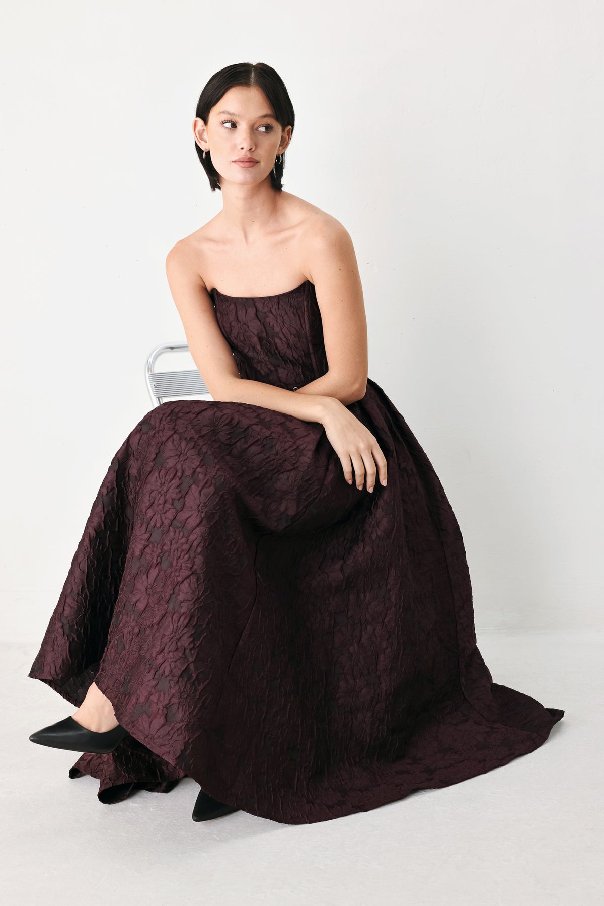 A woman models a strapless burgundy A-line gown with a textured jacquard bodice and a matching beaded waistband | FREEMARKET