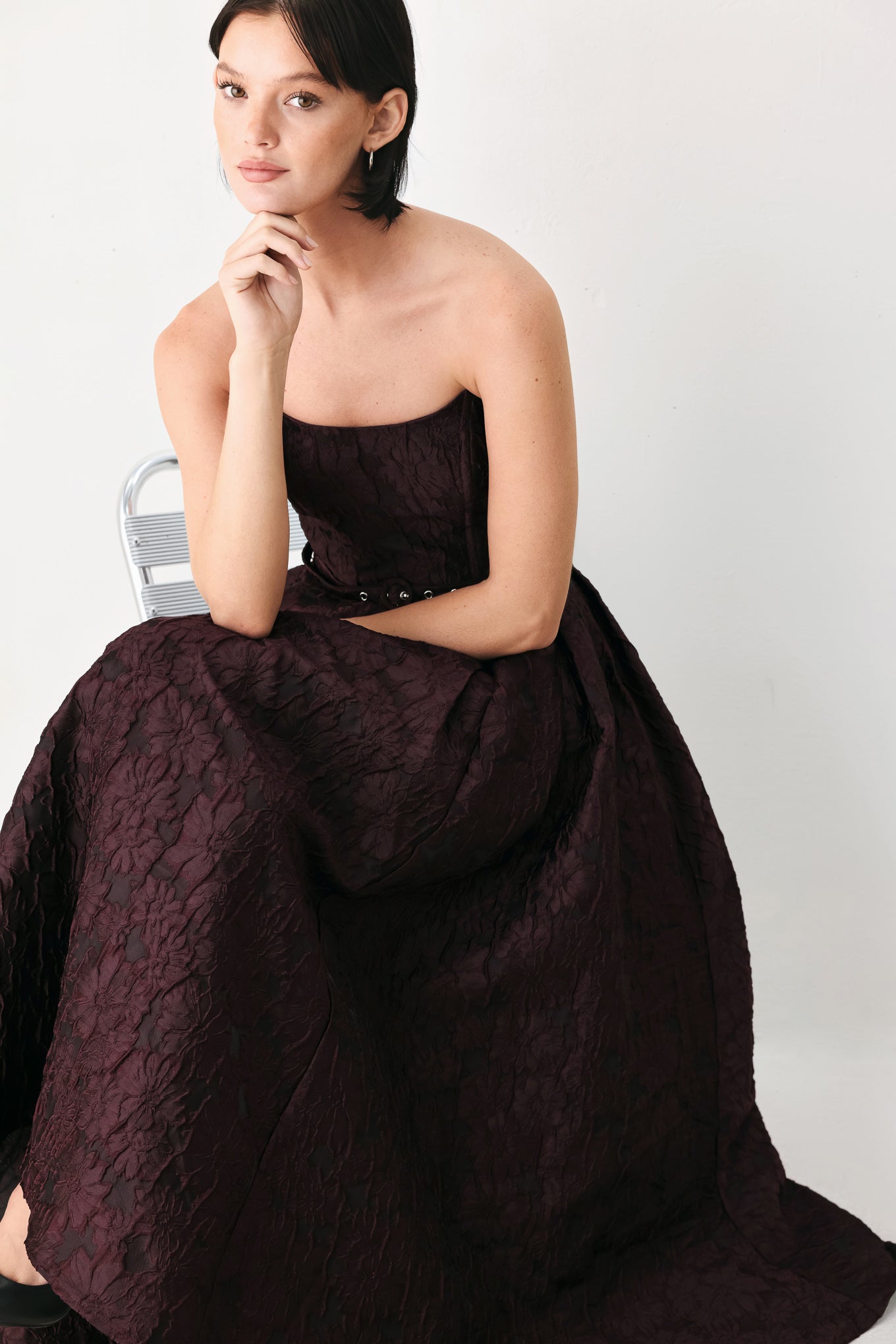 A woman models a strapless burgundy A-line gown with a textured jacquard bodice and a matching beaded waistband | FREEMARKET