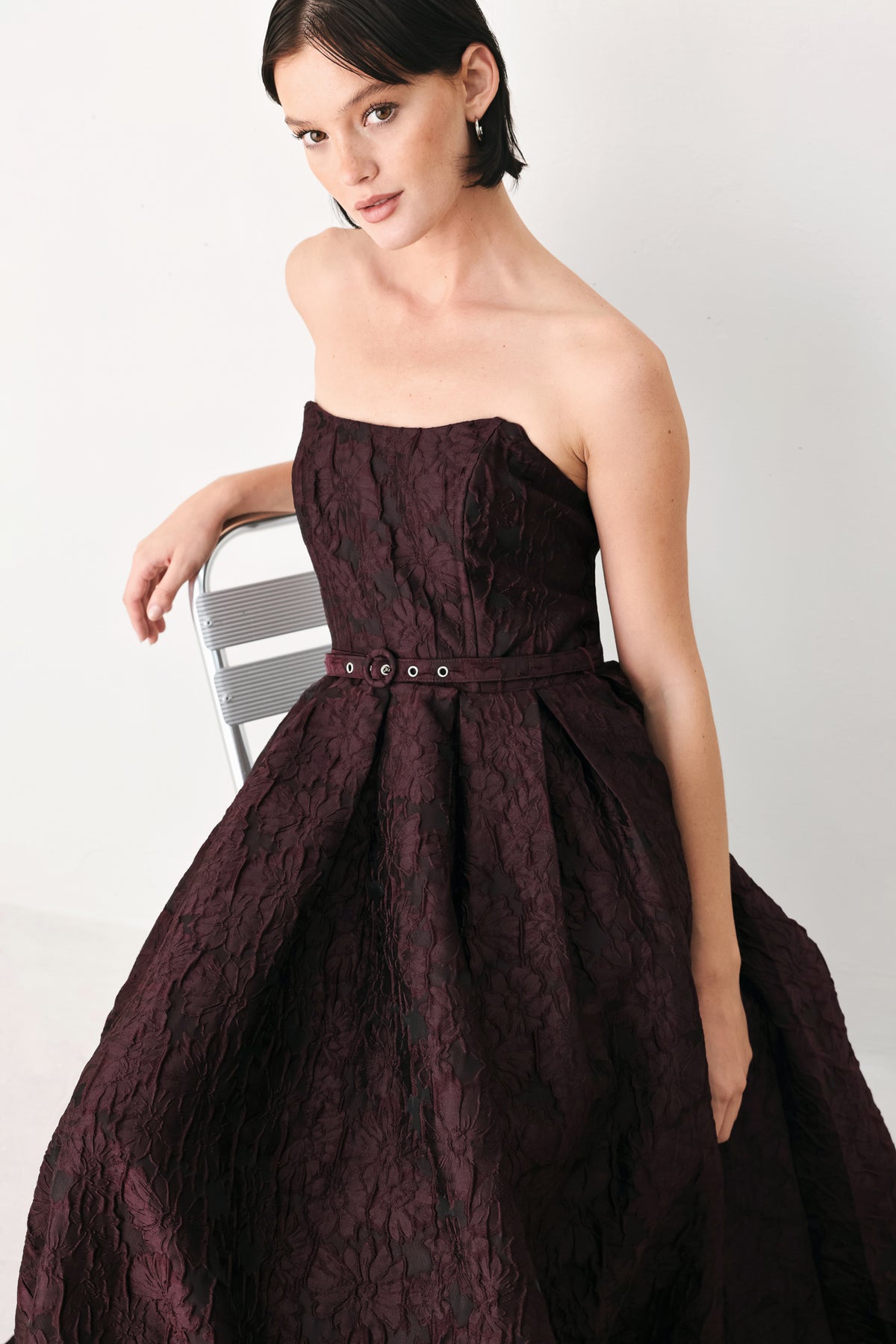 A woman models a strapless burgundy A-line gown with a textured jacquard bodice and a matching beaded waistband | FREEMARKET