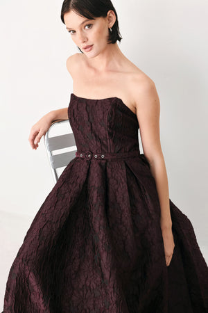 A woman models a strapless burgundy A-line gown with a textured jacquard bodice and a matching beaded waistband | FREEMARKET