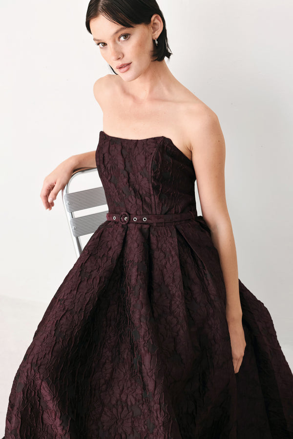 A woman models a strapless burgundy A-line gown with a textured jacquard bodice and a matching beaded waistband | FREEMARKET