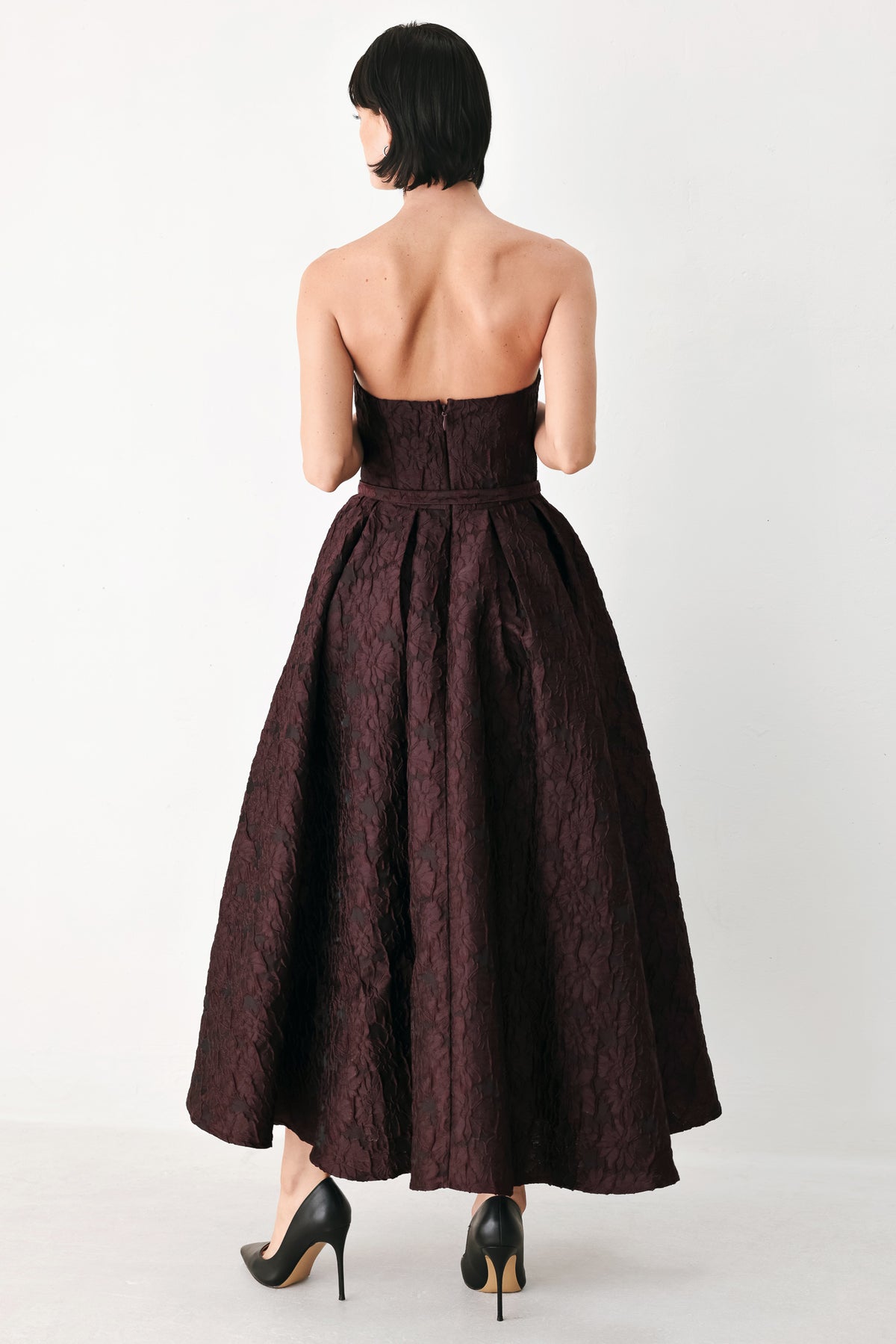 A woman models a strapless burgundy A-line gown with a textured jacquard bodice and a matching beaded waistband | FREEMARKET